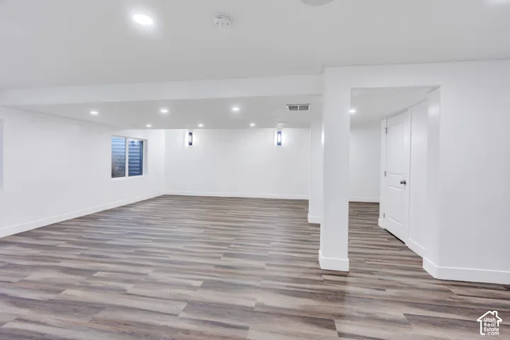 Expansive room featuring wood-finish flooring, recessed lighting, white walls, and built-in doors