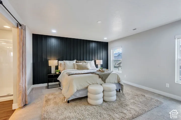Accent wall with vertical paneling, recessed lighting, carpeted flooring, two windows, and a sliding barn door leading to a shower enclosure