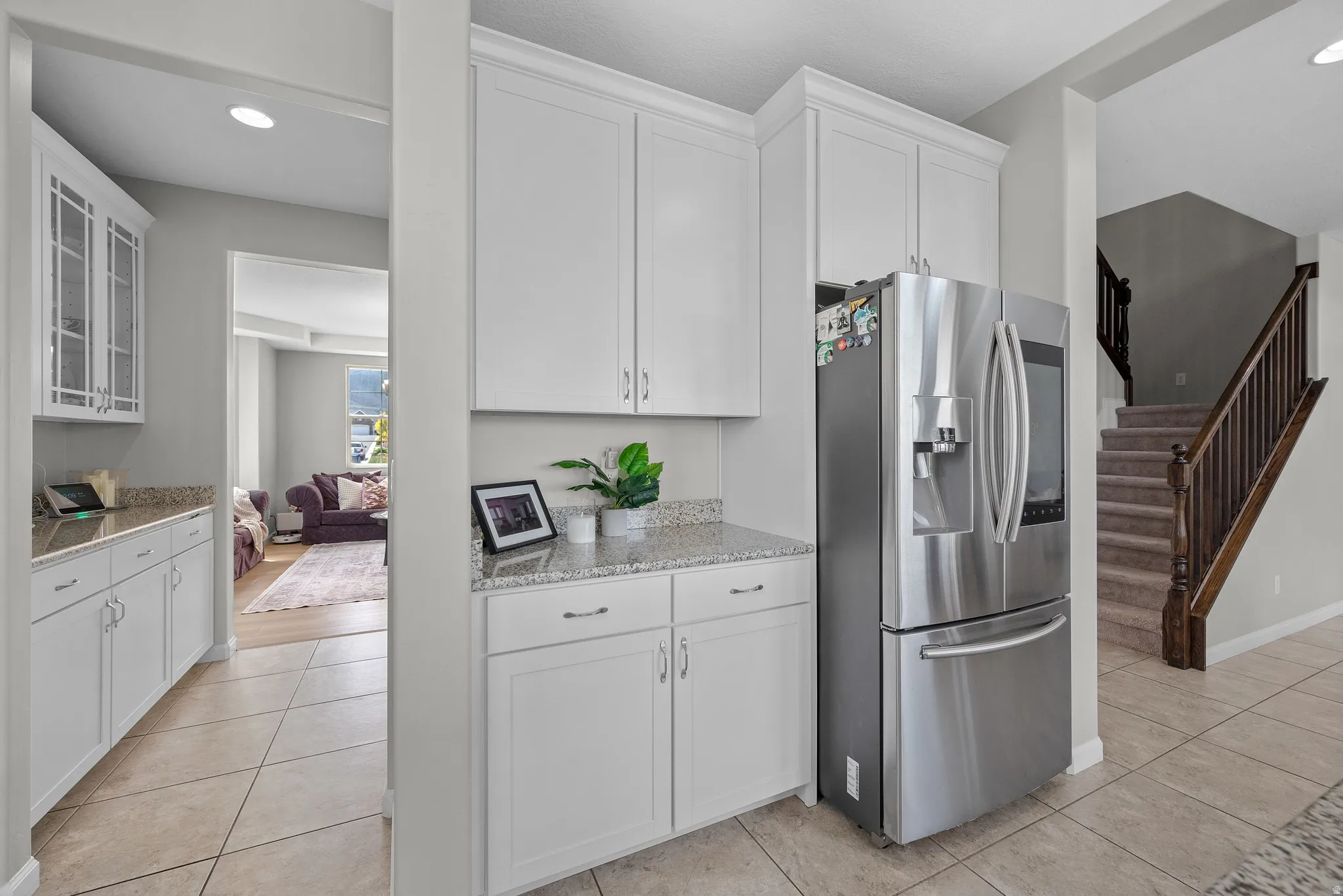 Kitchen featuring recessed lighting, stainless steel fridge, white cabinets, light stone counters, and light tile patterned flooring