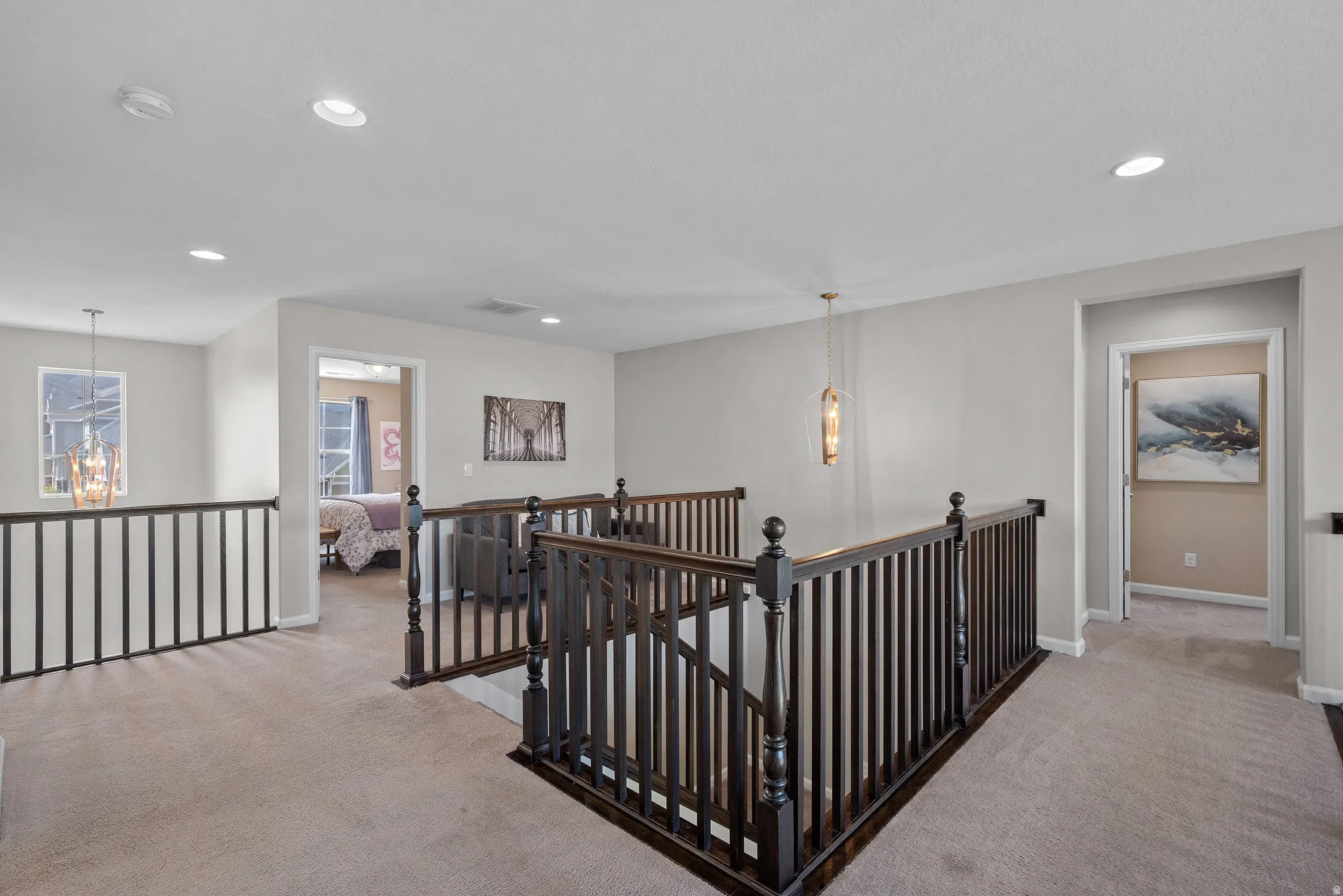 Hallway with an upstairs landing, suspended lighting, and light carpet