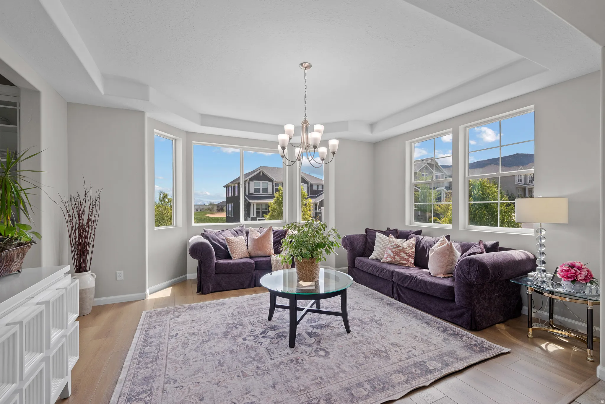 Living area featuring a tray ceiling, suspended lighting, and light wood-type flooring