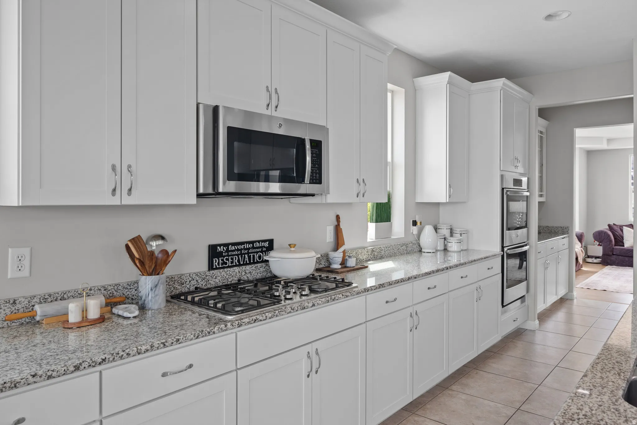 Kitchen with white cabinets, stainless steel appliances, light stone counters, light tile patterned floors, and glass fronted cabinets