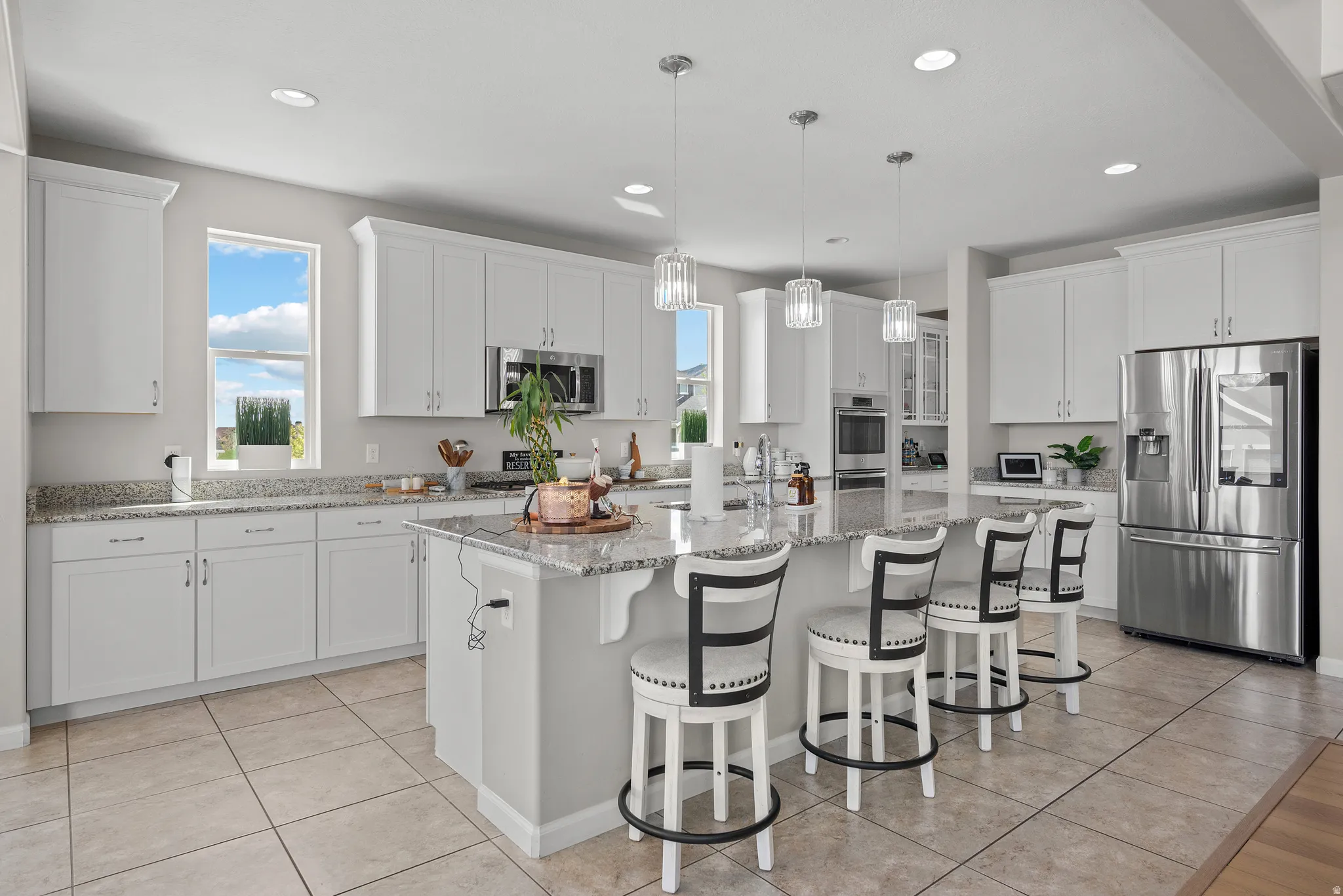 Kitchen with stainless steel appliances, white cabinetry, a kitchen island with sink, and light stone countertops