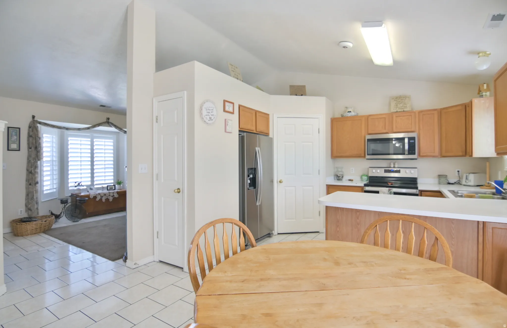 Kitchen featuring light tile patterned floors, light countertops, stainless steel appliances, vaulted ceiling, and a peninsula