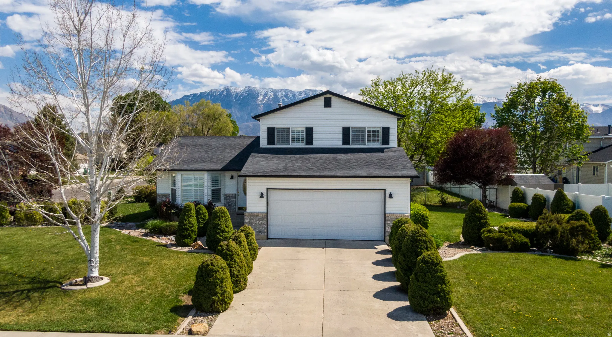 Traditional-style house featuring a front lawn, concrete driveway, an attached garage, a mountain view, and stone siding