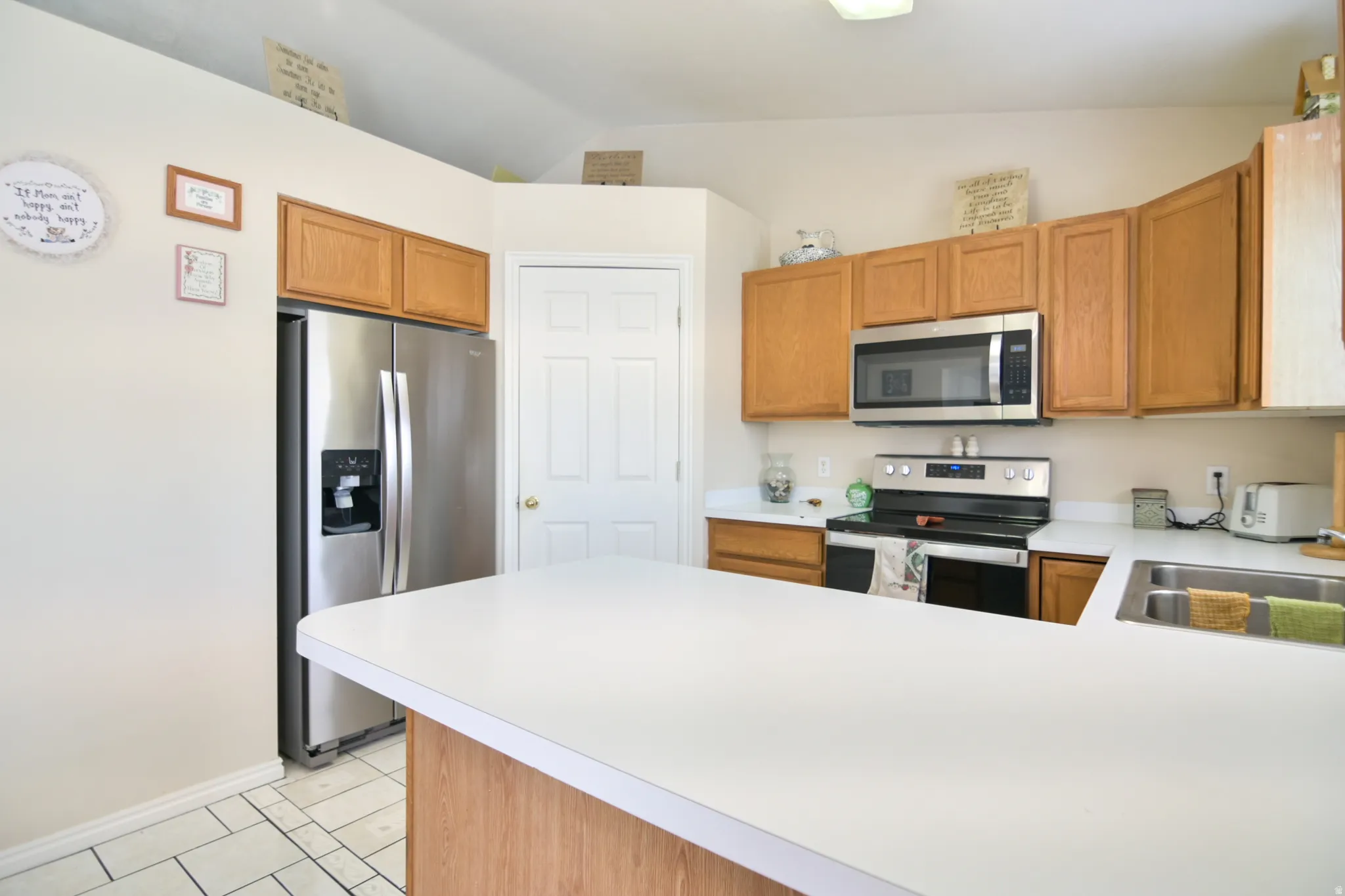 Kitchen with light countertops, stainless steel appliances, a peninsula, light tile patterned floors, and wood finish cabinetry