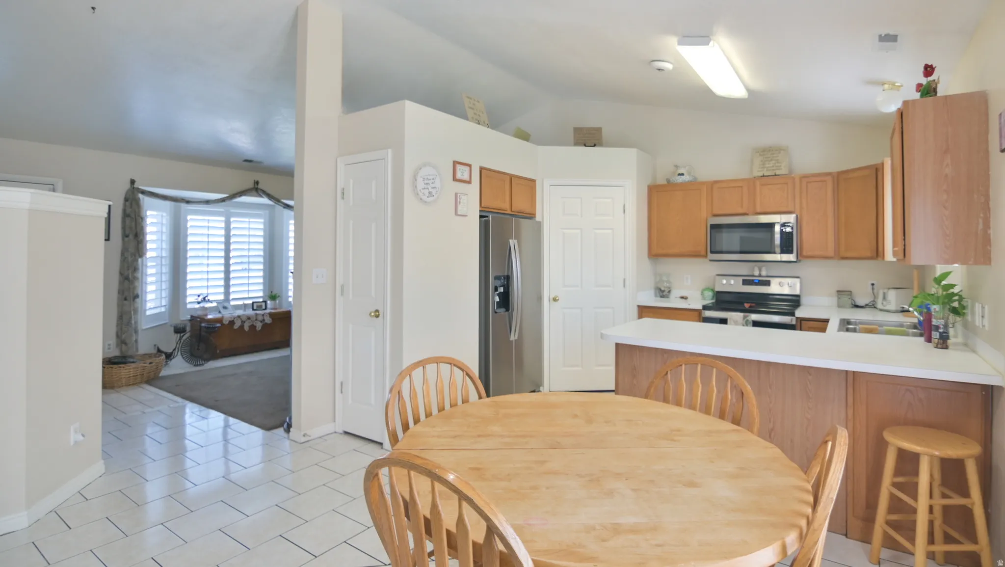 Kitchen with light countertops, a peninsula, stainless steel appliances, light tile patterned floors, and a breakfast bar