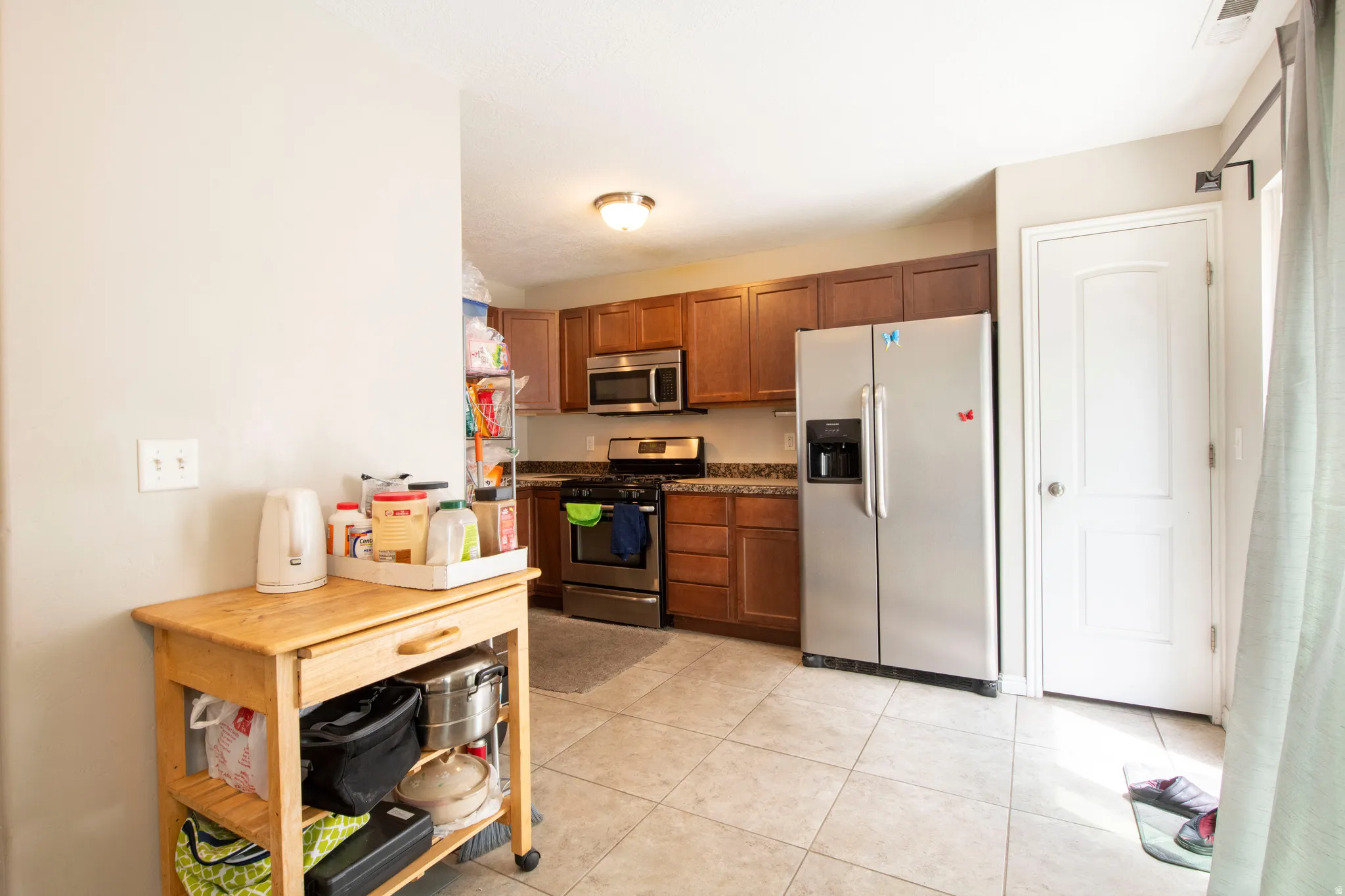 Kitchen with stainless steel appliances, wood finish cabinets, and light tile patterned floors