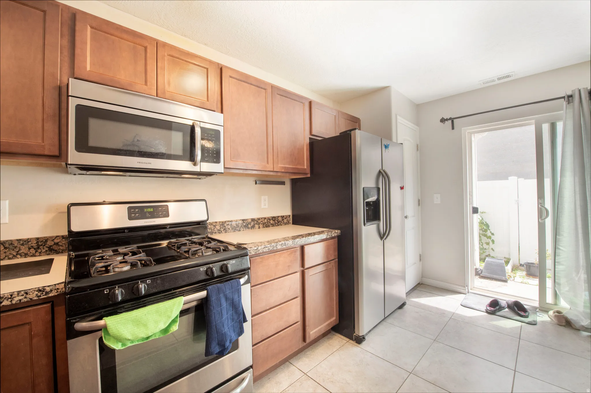 Kitchen with stainless steel appliances, wood finish cabinetry, and light tile patterned floors