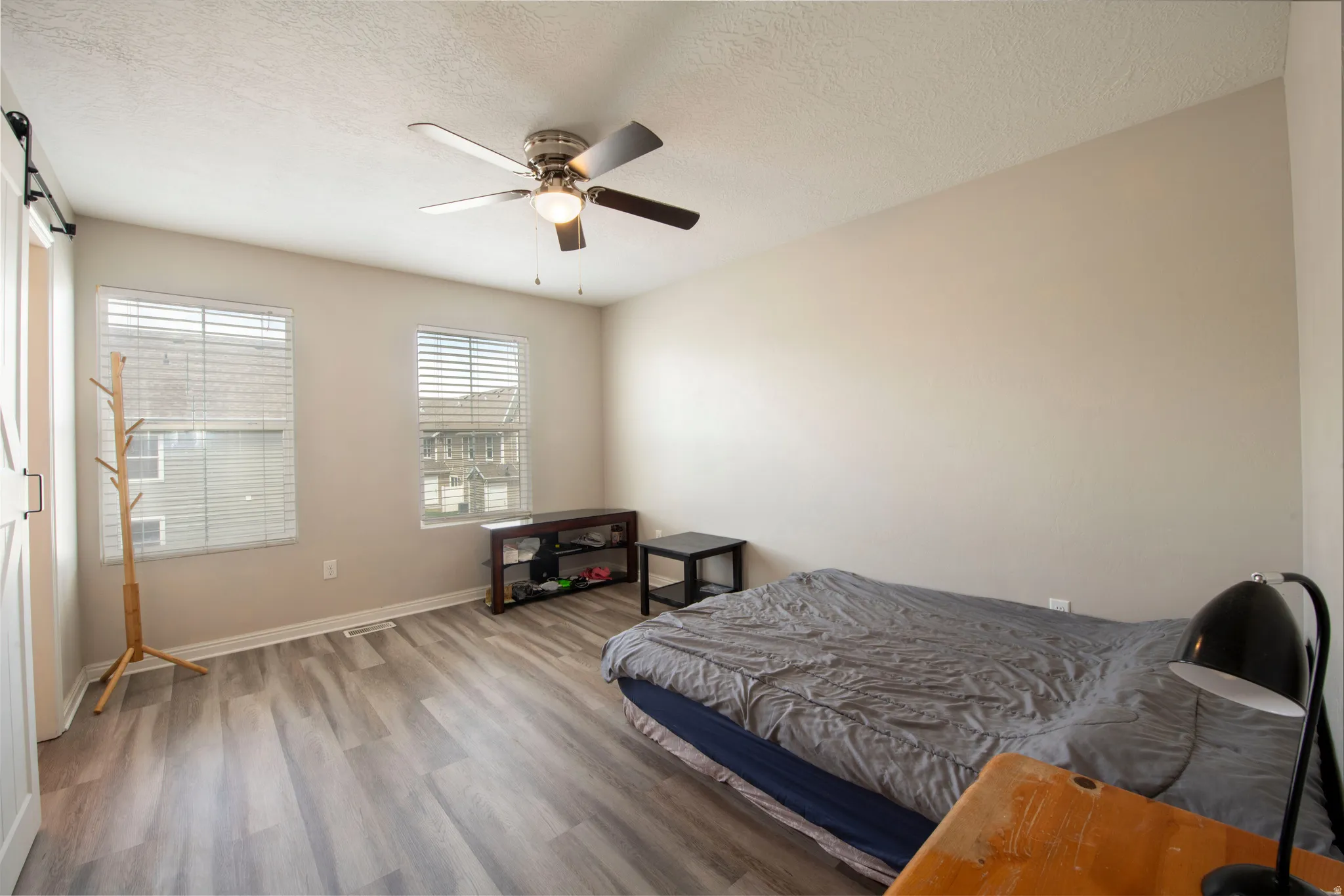 Bedroom featuring wood finished floors, a barn door, a textured ceiling, and a ceiling fan