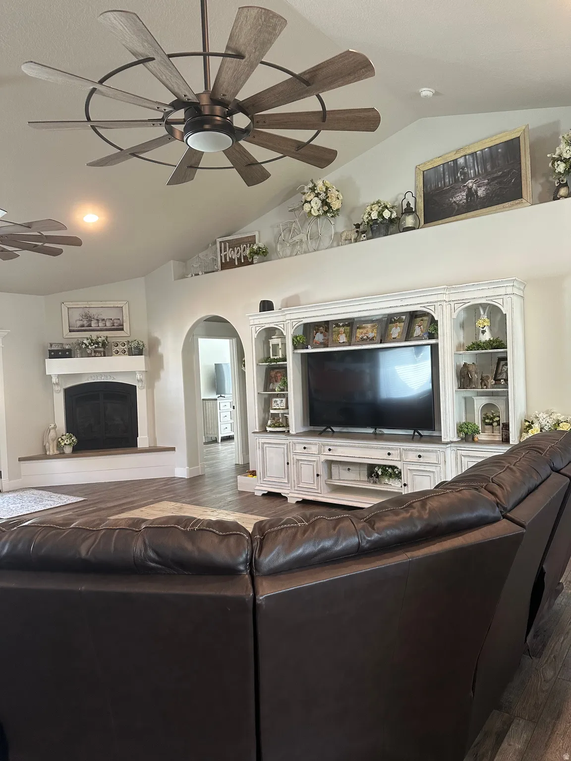 Living room featuring hardwood / wood-style flooring, a ceiling fan, vaulted ceiling, a glass covered fireplace, and arched walkways