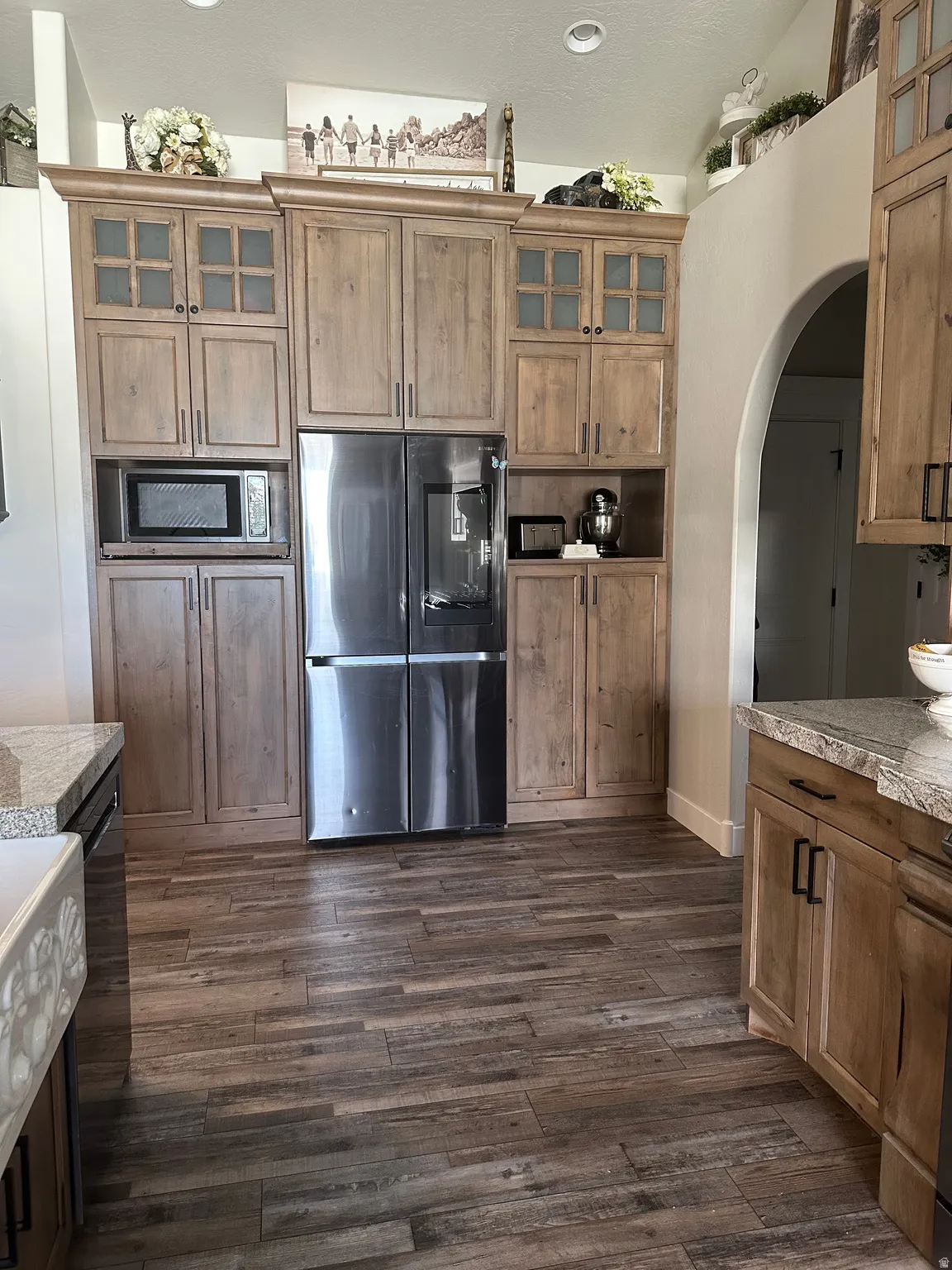 Kitchen with glass fronted cabinets, stainless steel appliances, wood finish cabinetry, light countertops, and dark wood-style flooring