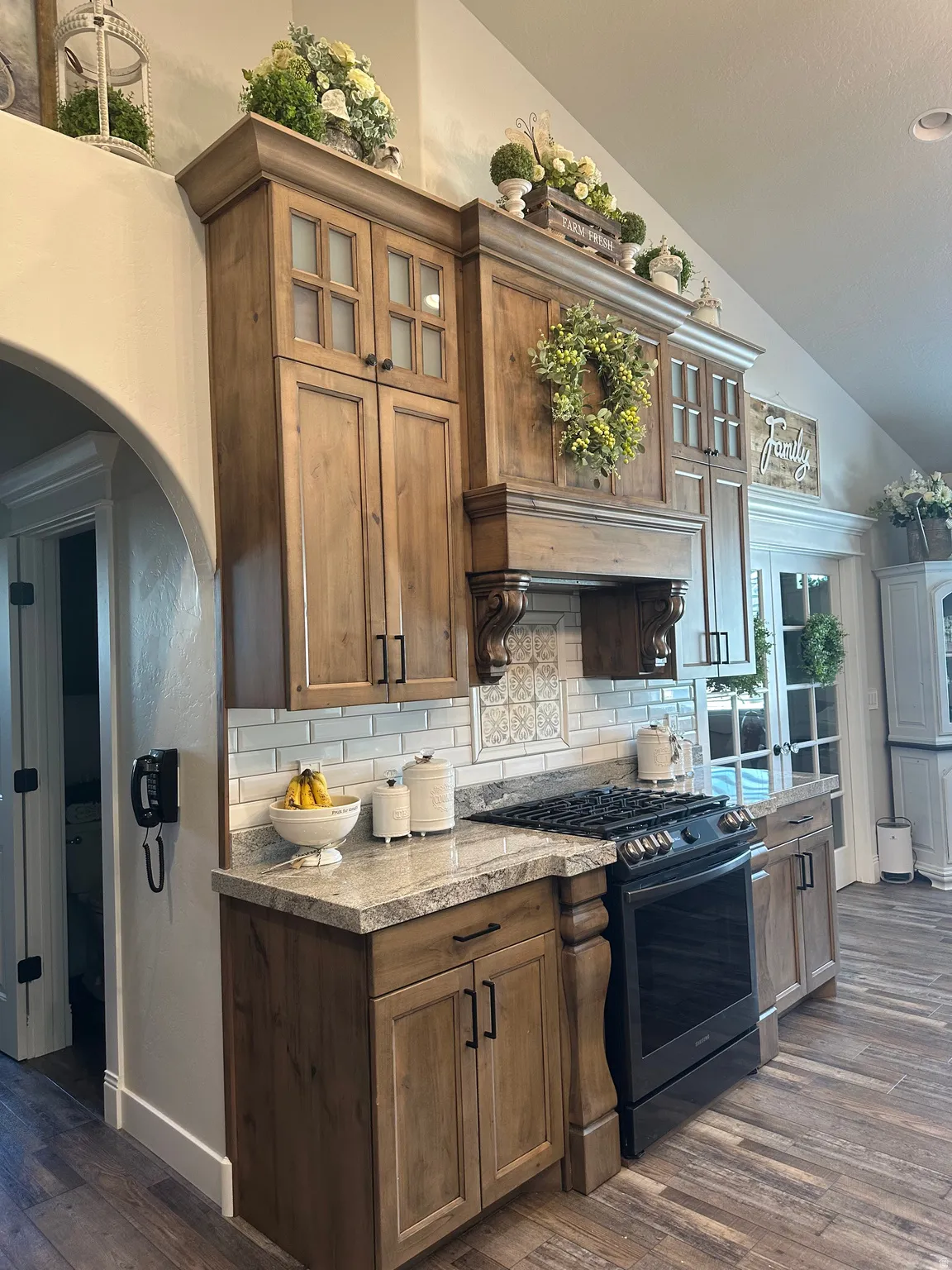 Kitchen featuring dark wood finished floors, glass insert cabinets, backsplash, black range with gas stovetop, and vaulted ceiling
