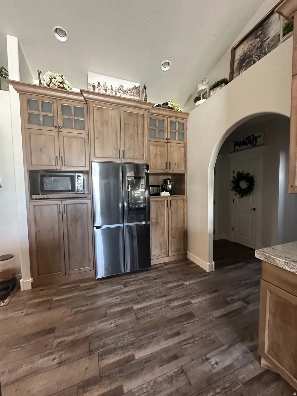 Kitchen featuring freestanding refrigerator, arched walkways, glass insert cabinets, wood finish cabinetry, and dark wood-style floors