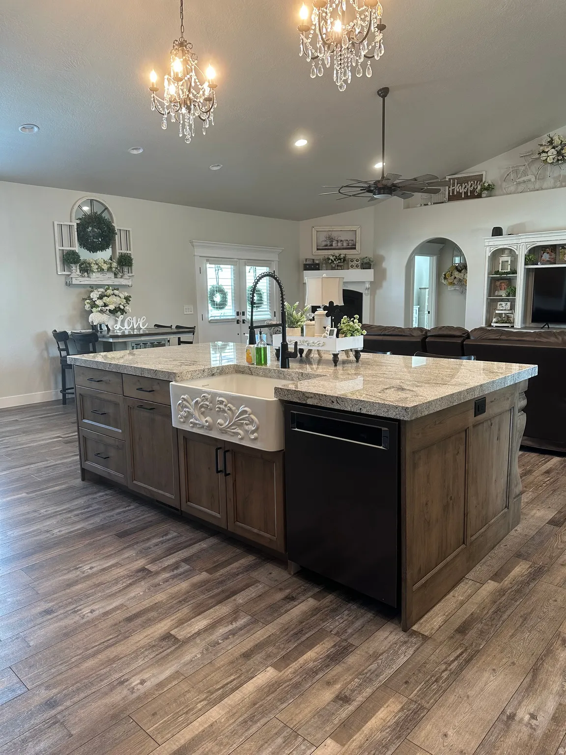 Kitchen featuring open floor plan, black dishwasher, an island with sink, light stone countertops, and dark wood finished floors