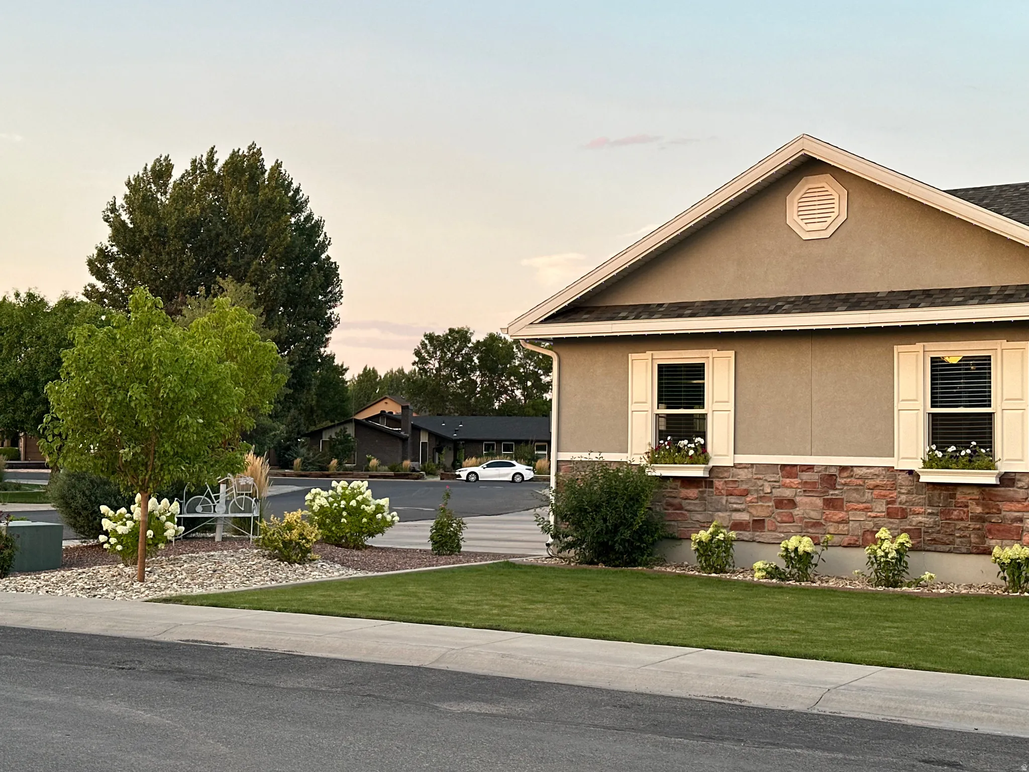 View of side of home with stucco siding, stone siding, a yard, and a shingled roof