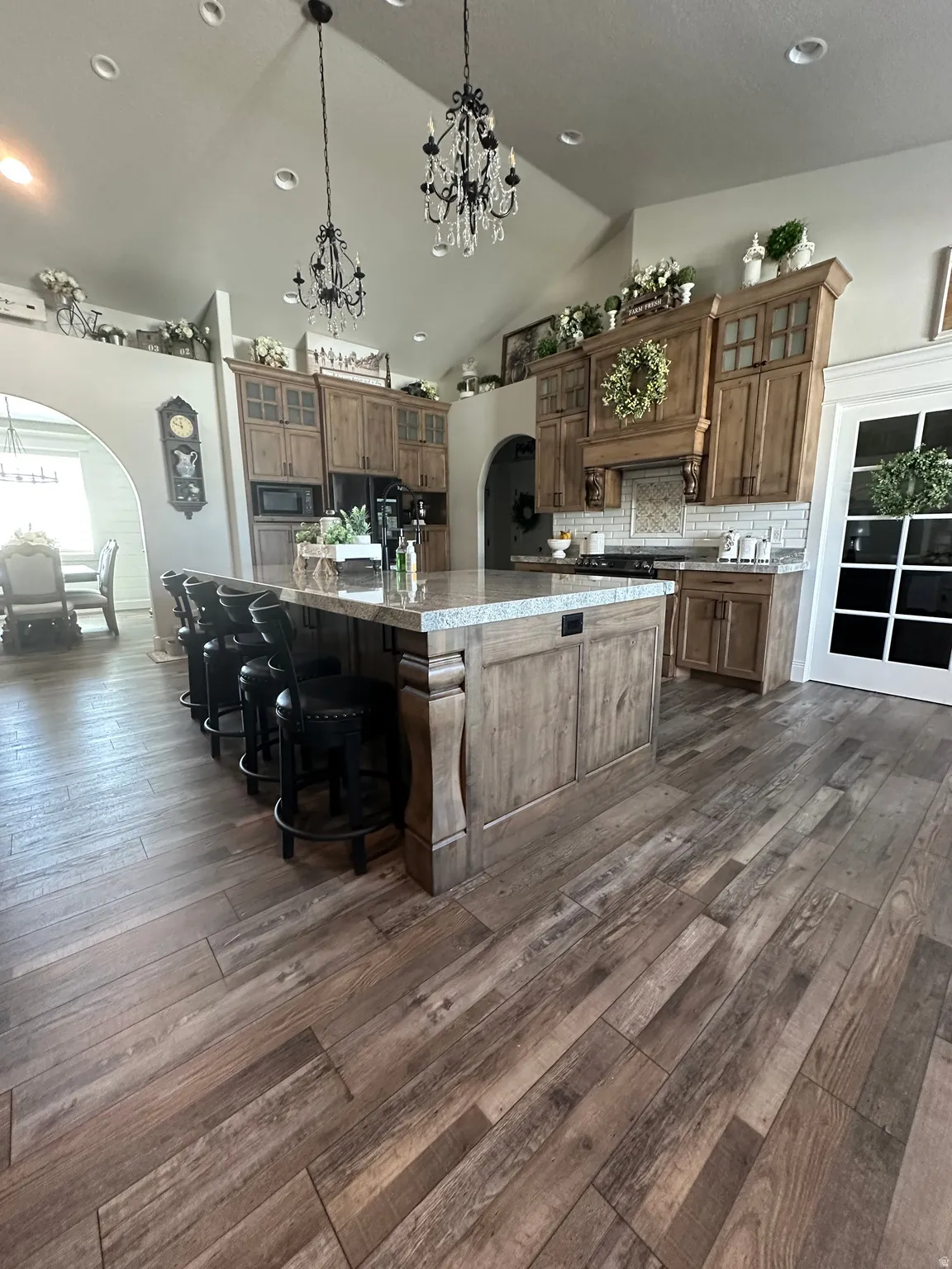 Kitchen featuring arched walkways, glass insert cabinets, a breakfast bar area, dark wood-style flooring, and lofted ceiling