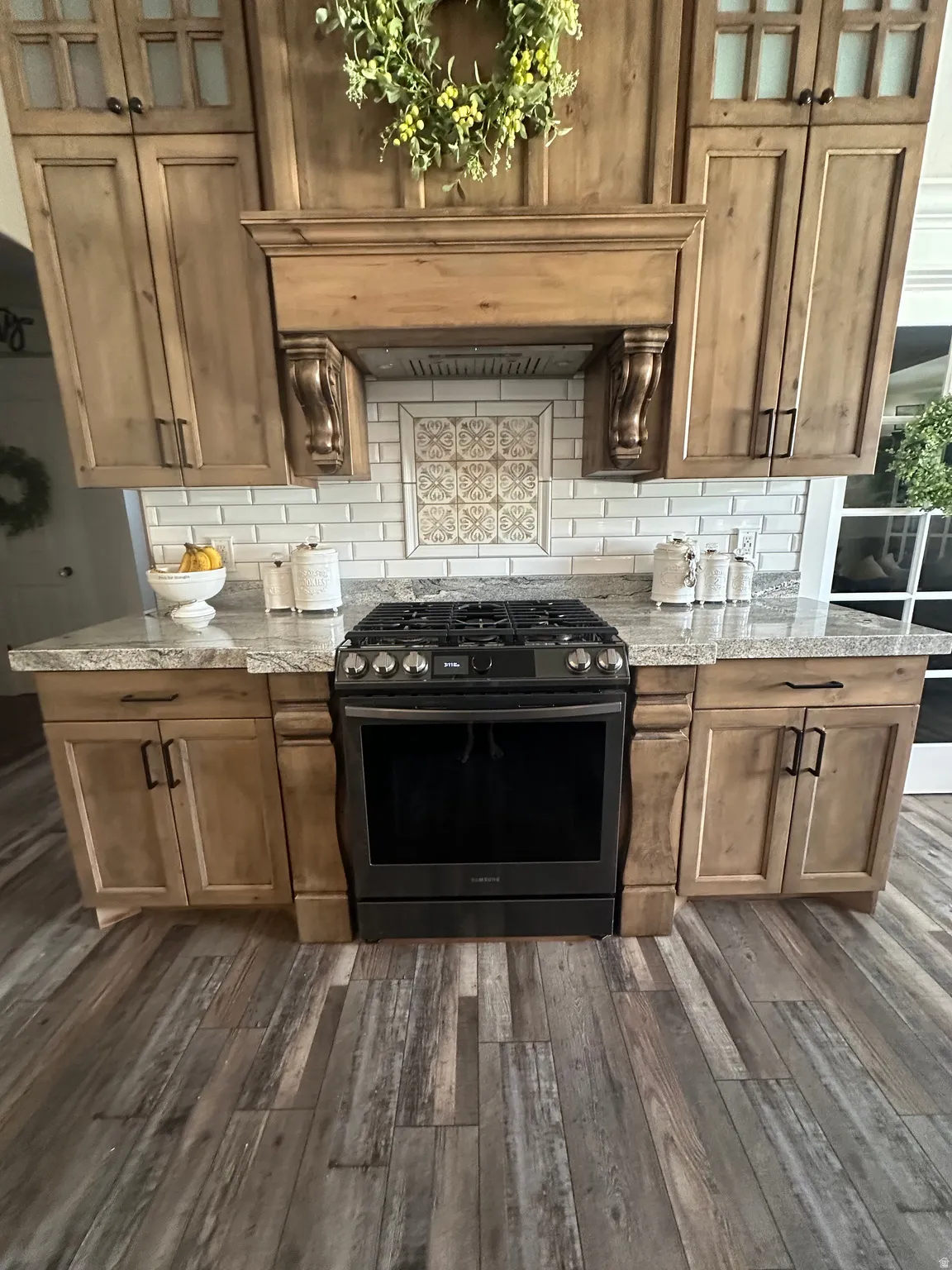 Kitchen with gas range, backsplash, light stone countertops, and glass fronted cabinets