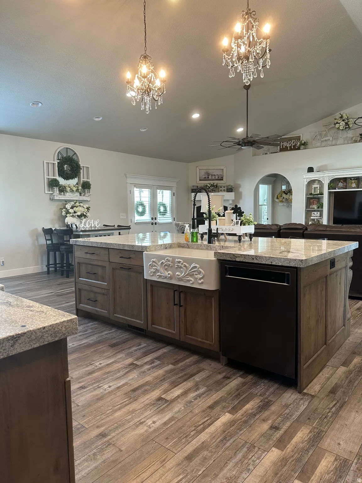Kitchen with open floor plan, light stone countertops, dark wood-style floors, dishwasher, and a center island with sink
