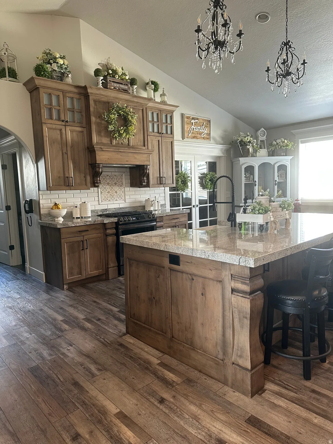 Kitchen featuring arched walkways, dark wood finished floors, wood finish cabinets, and glass insert cabinets