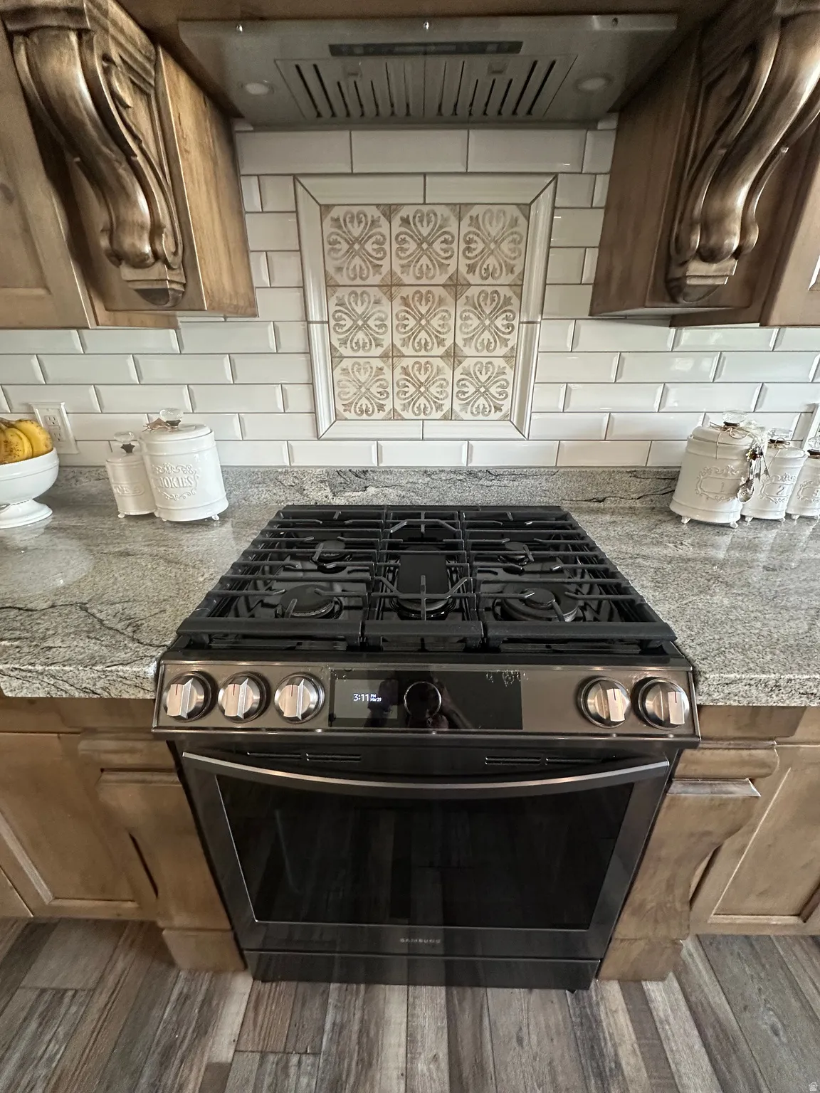 Kitchen view of exhaust hood, light stone counters, black gas range, and tasteful backsplash