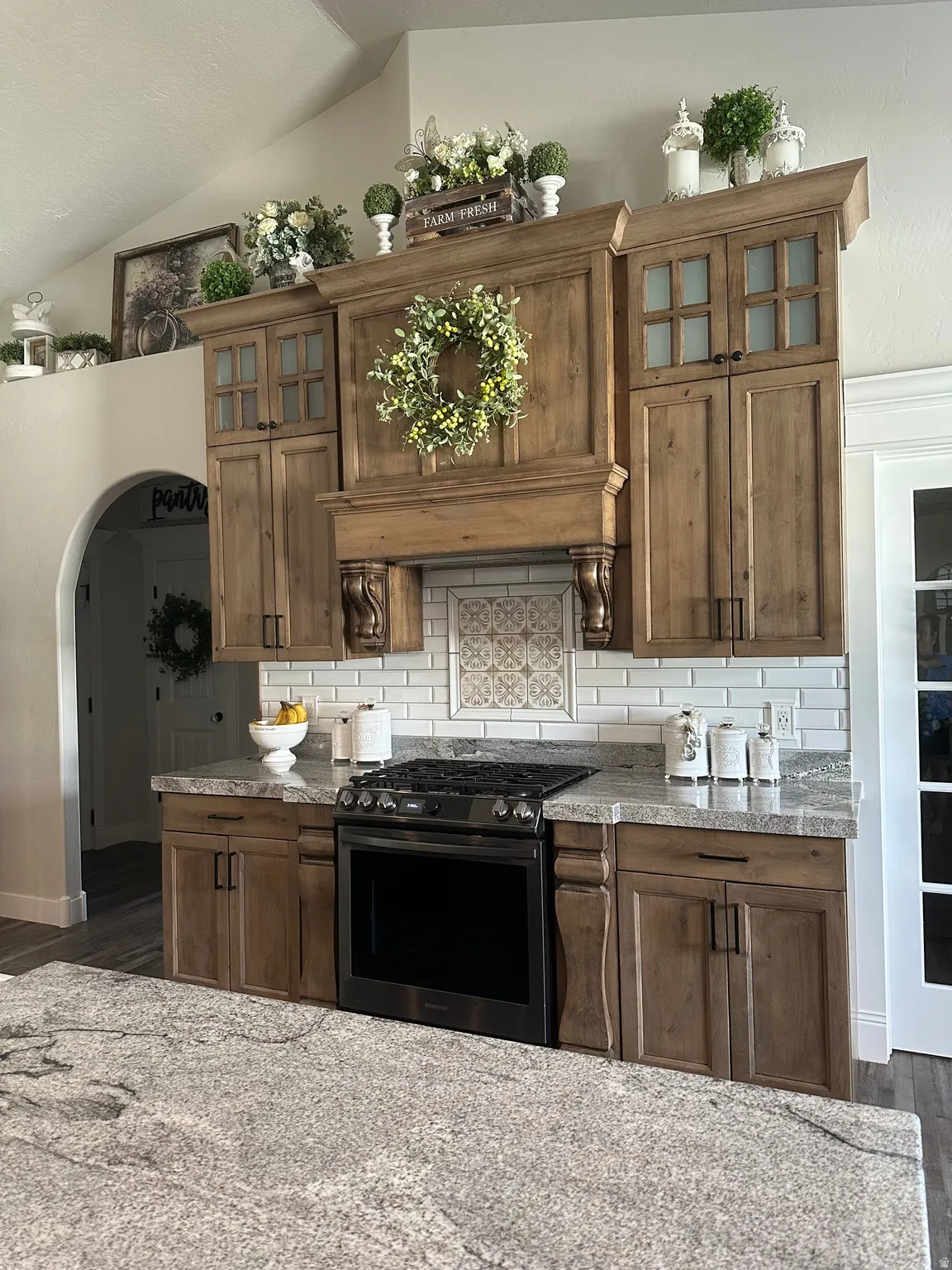 Kitchen featuring glass fronted cabinets, stainless steel range with gas cooktop, dark wood-type flooring, arched walkways, and wood finish cabinets