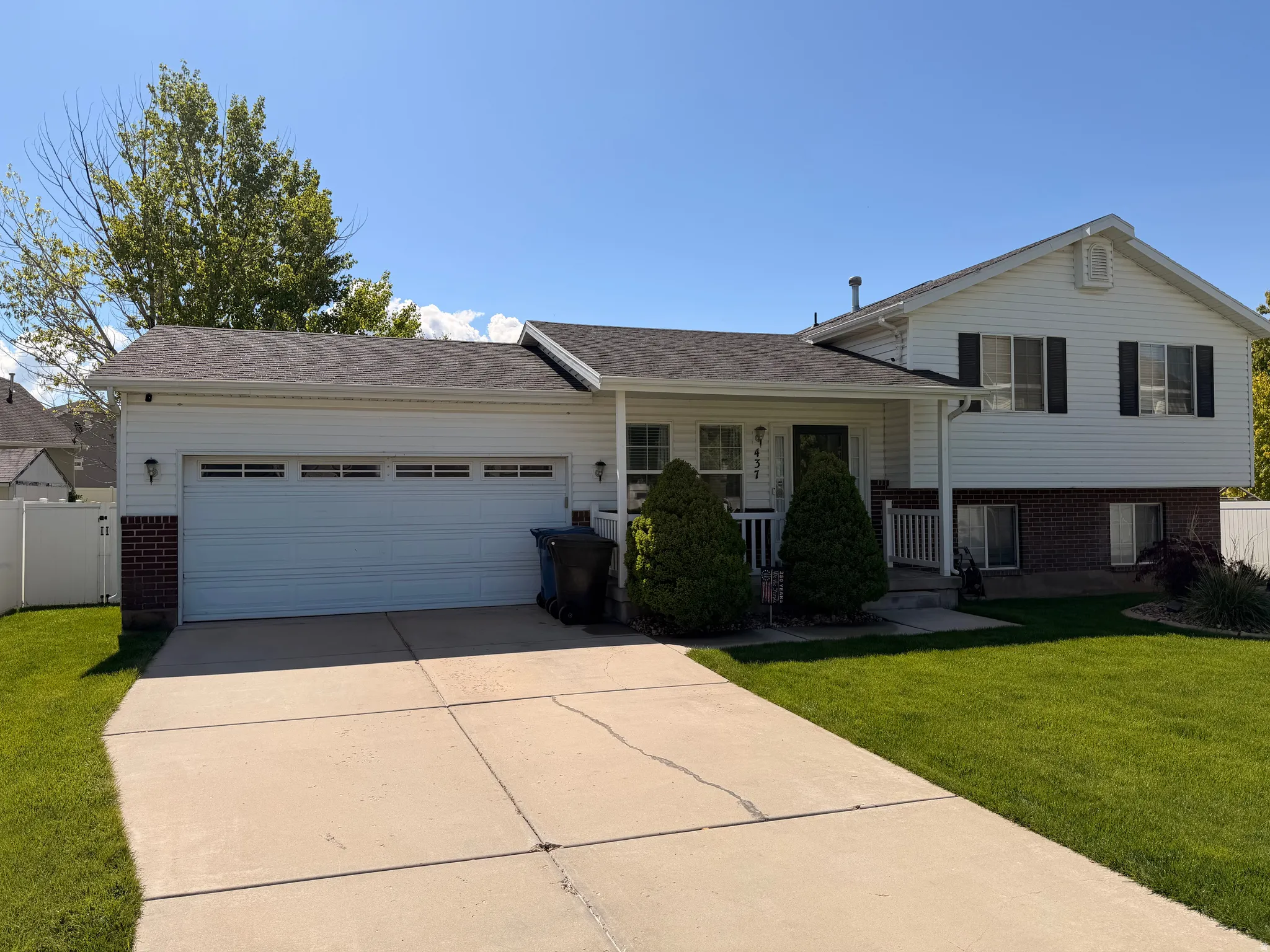 Tri-level home featuring brick siding, covered porch, an attached garage, and driveway
