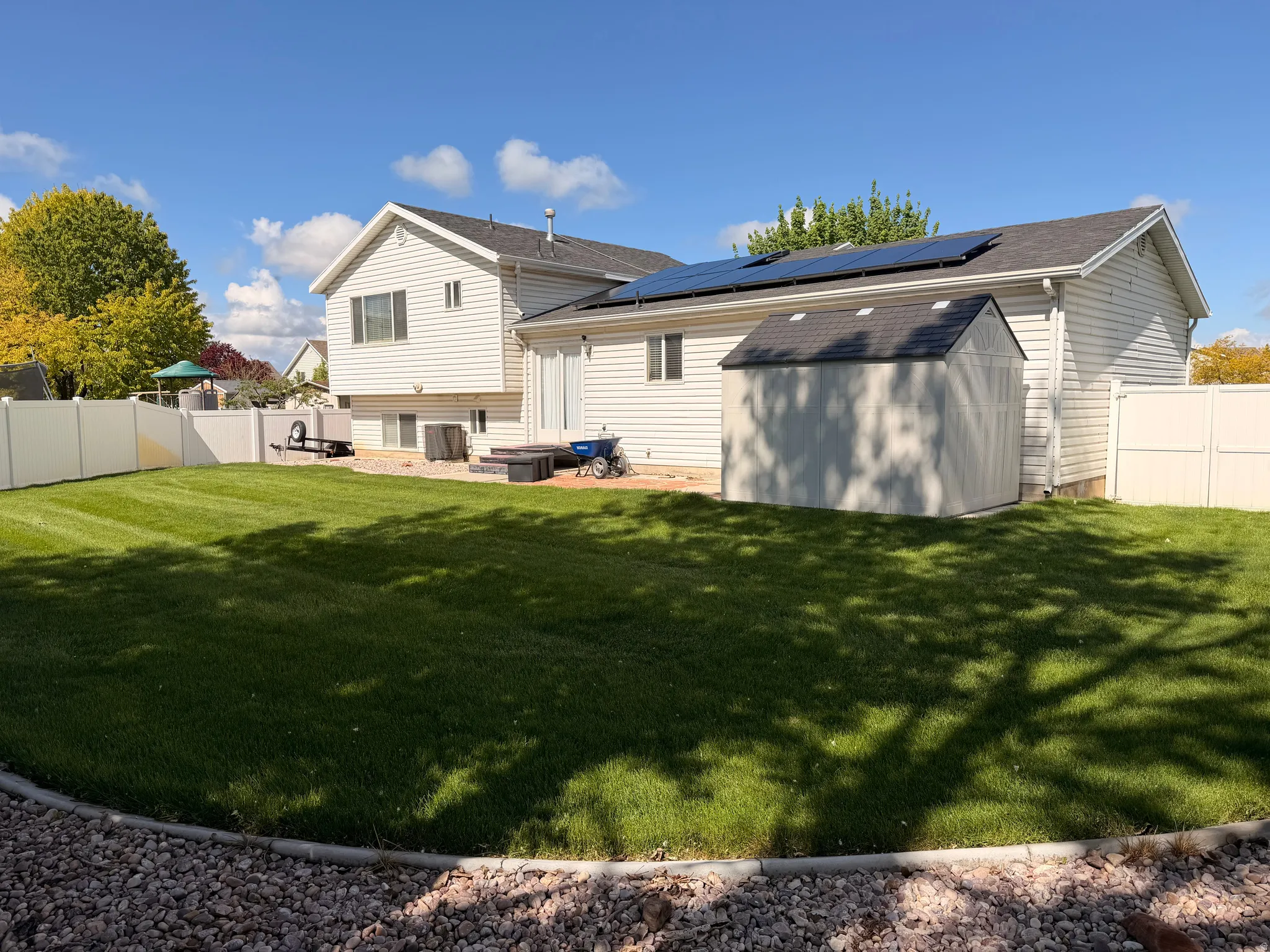 Rear view of property with a storage shed, a fenced backyard, and solar panels