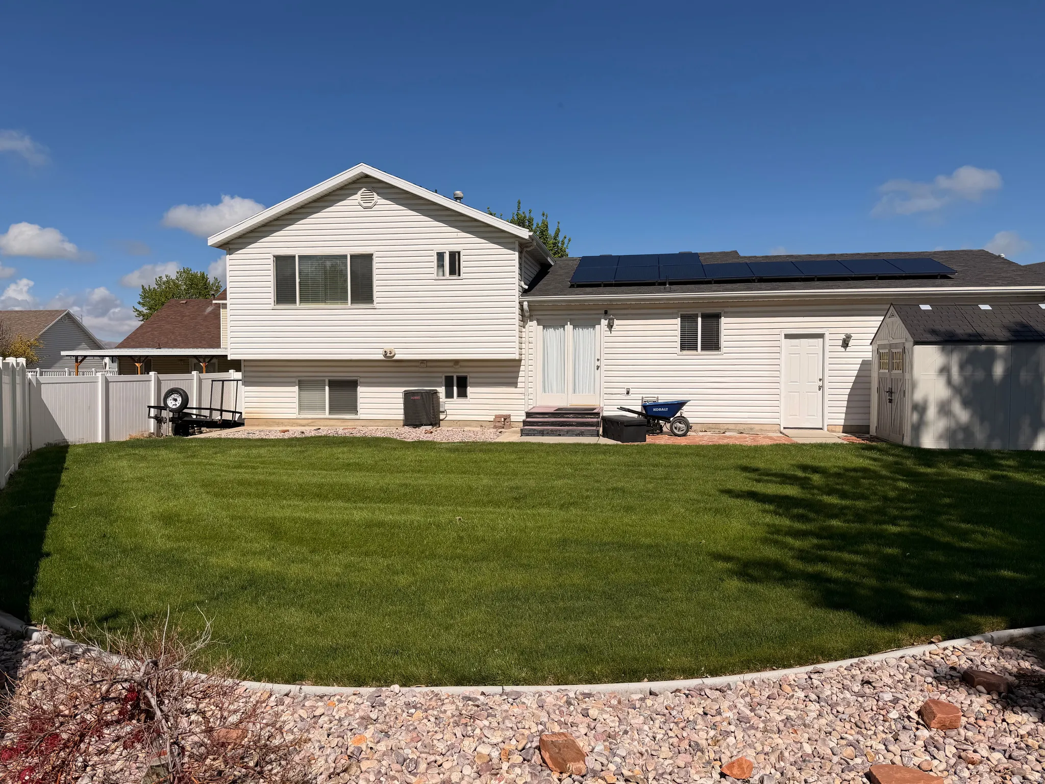 Rear view of property featuring a shed, roof mounted solar panels, entry steps, and roof with shingles