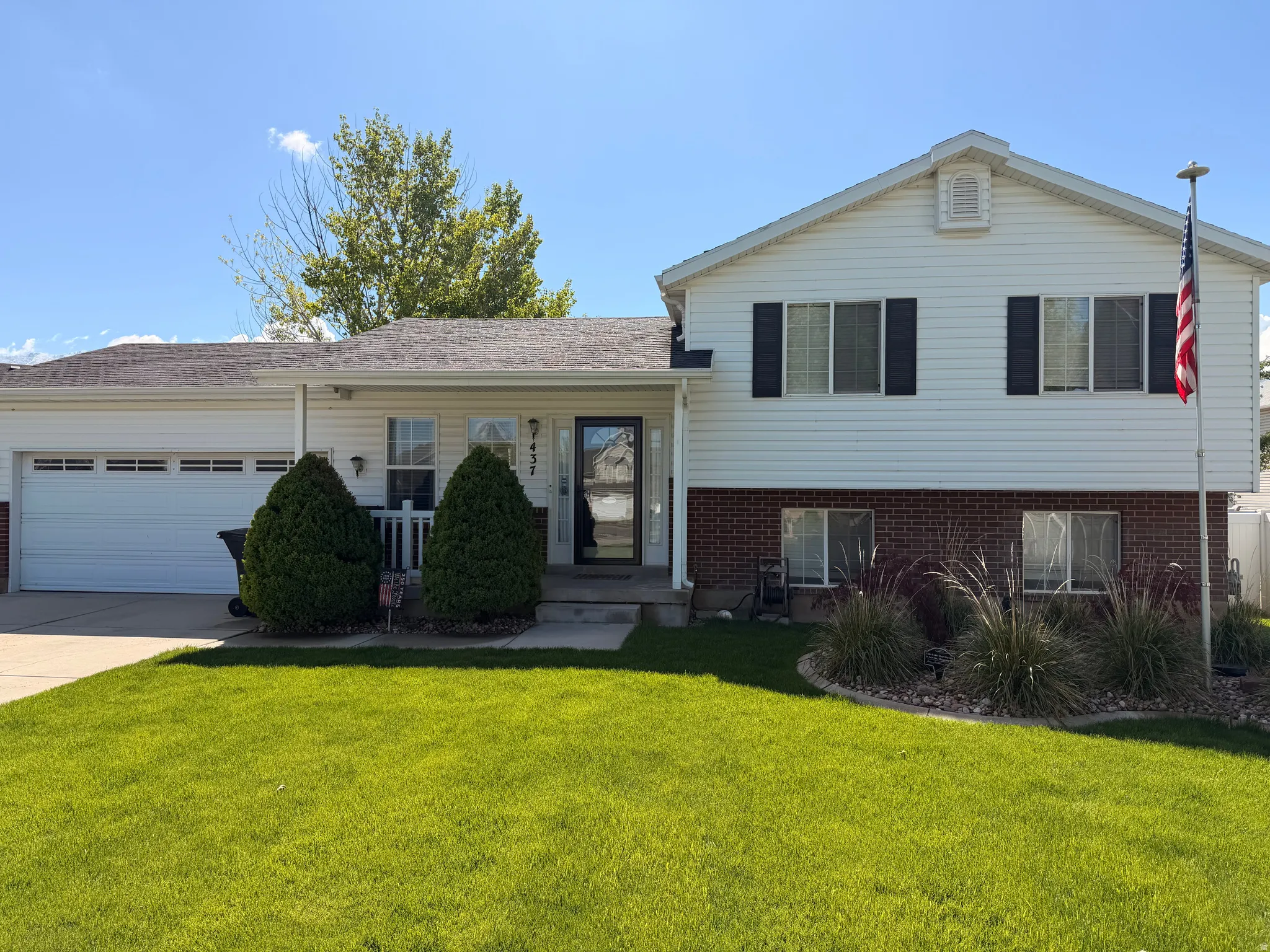 Split level home featuring brick siding, an attached garage, a front yard, concrete driveway, and a shingled roof