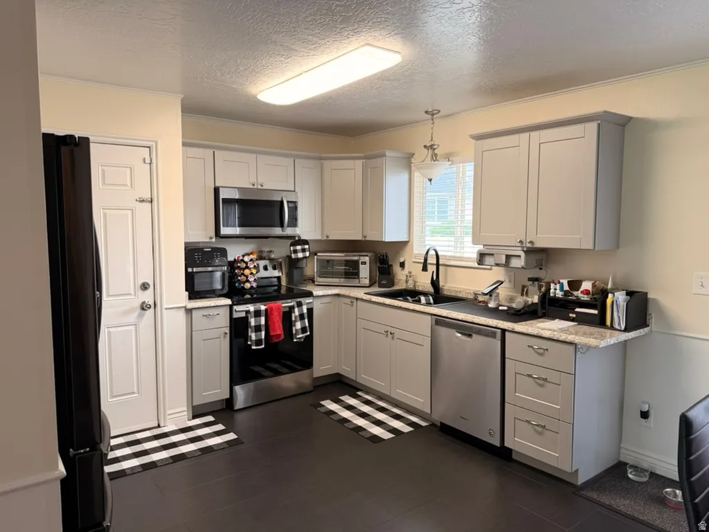 Kitchen with stainless steel appliances, a textured ceiling, dark wood finished floors, ornamental molding, and light stone countertops
