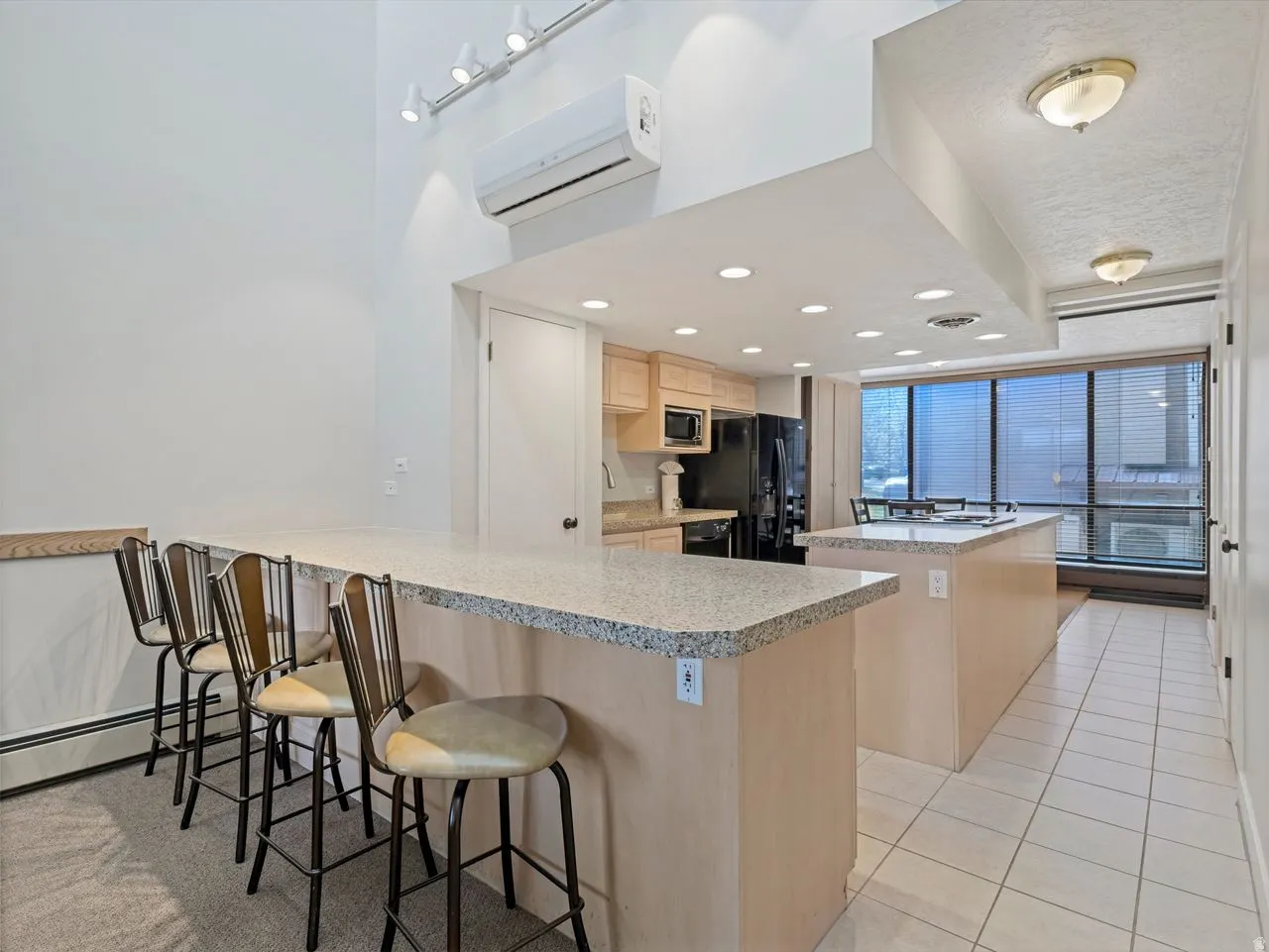 Kitchen featuring a kitchen breakfast bar, light wood finish cabinets, a peninsula, light tile patterned floors, and a center island