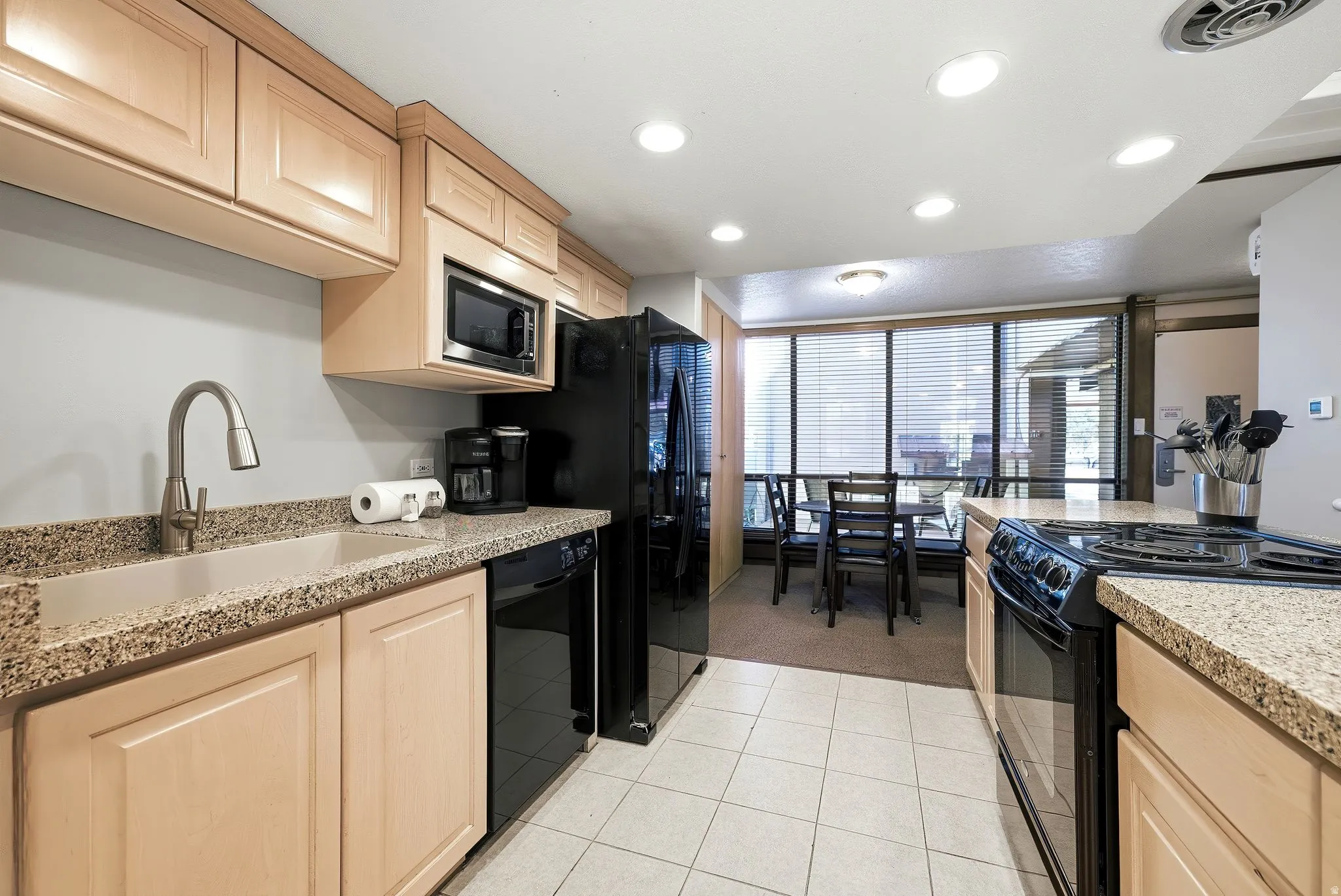Kitchen featuring light wood cabinetry, stone-finish countertops, and white tile flooring