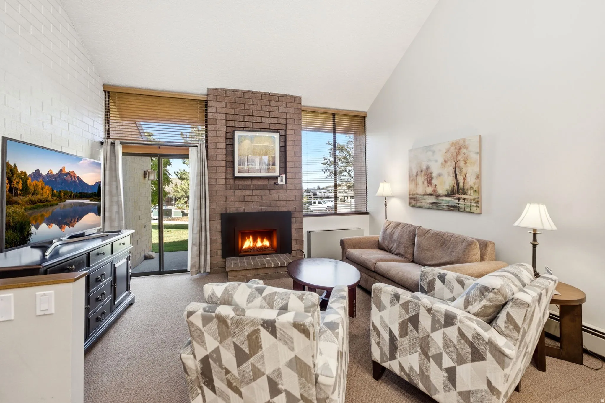 Living area featuring vaulted ceilings, a brick-surround fireplace with hearth, and durable carpet flooring