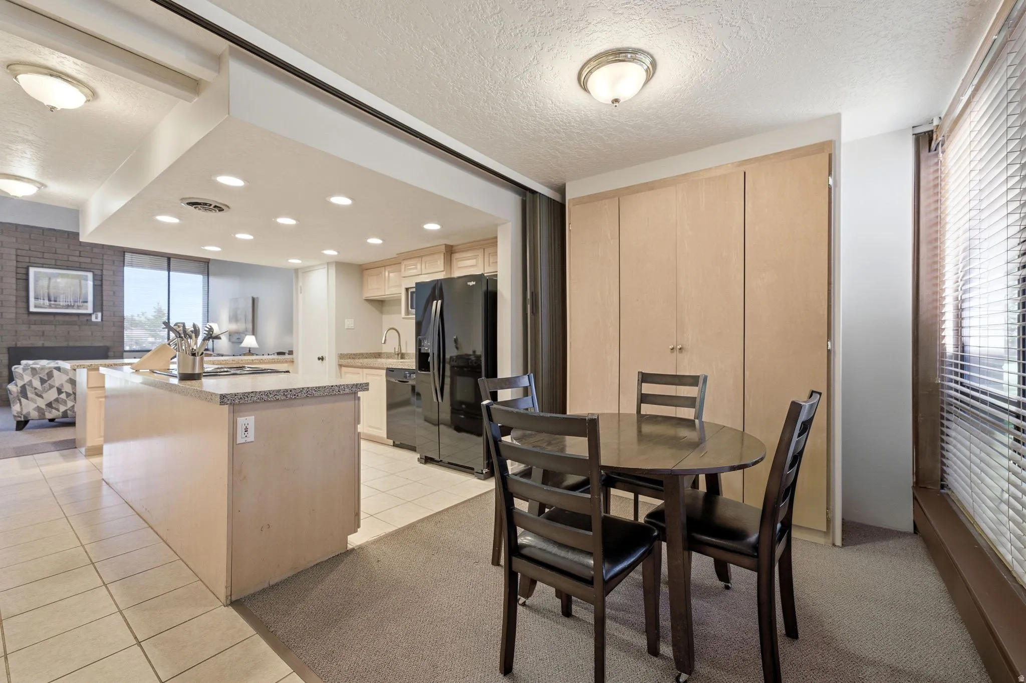 Kitchen and dining area featuring tile flooring, light-toned cabinetry, black appliances, recessed lighting, and a large window with blinds