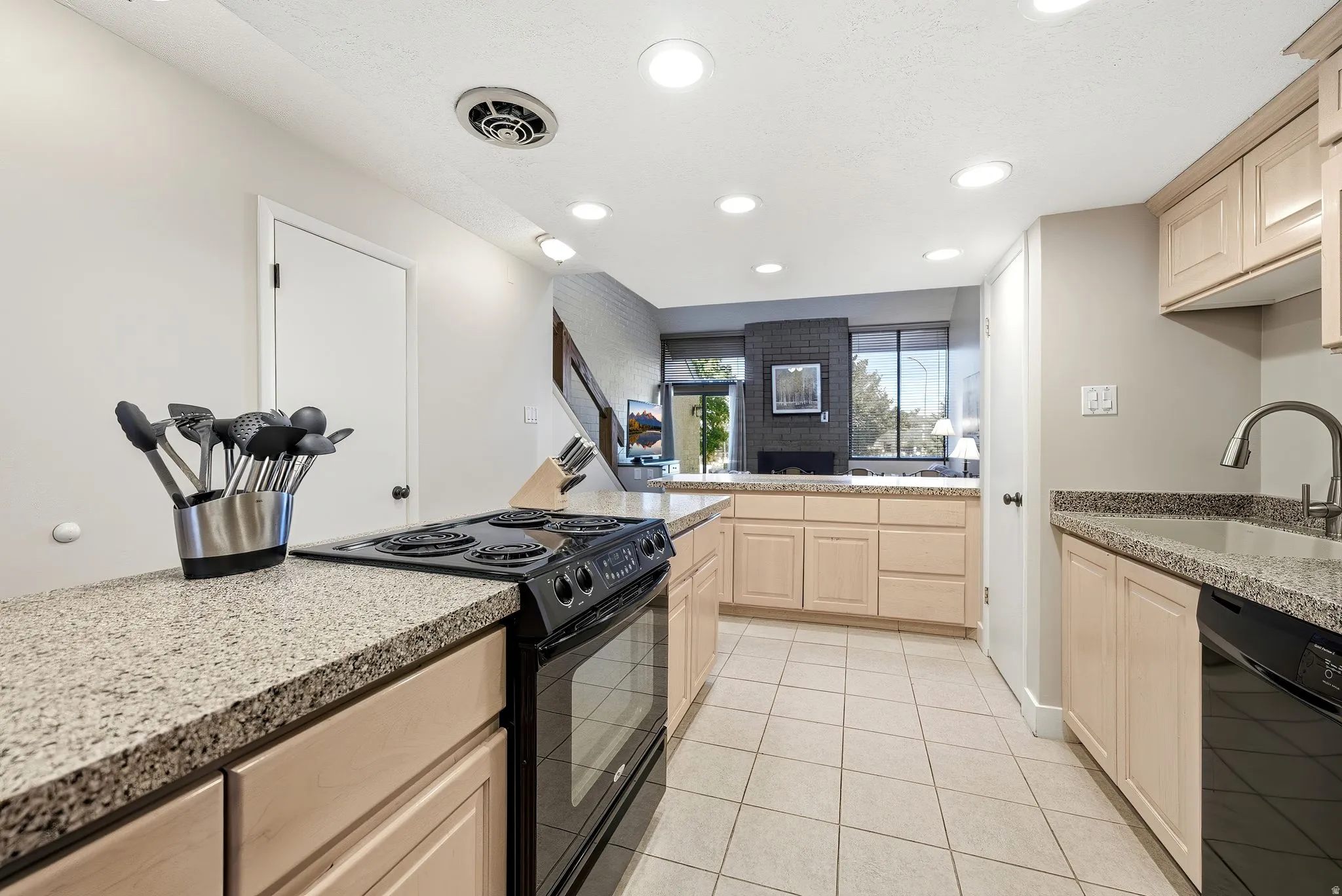 Kitchen featuring light wood-finish cabinetry, granite-style countertops, tile flooring, a black electric range, and a black dishwasher