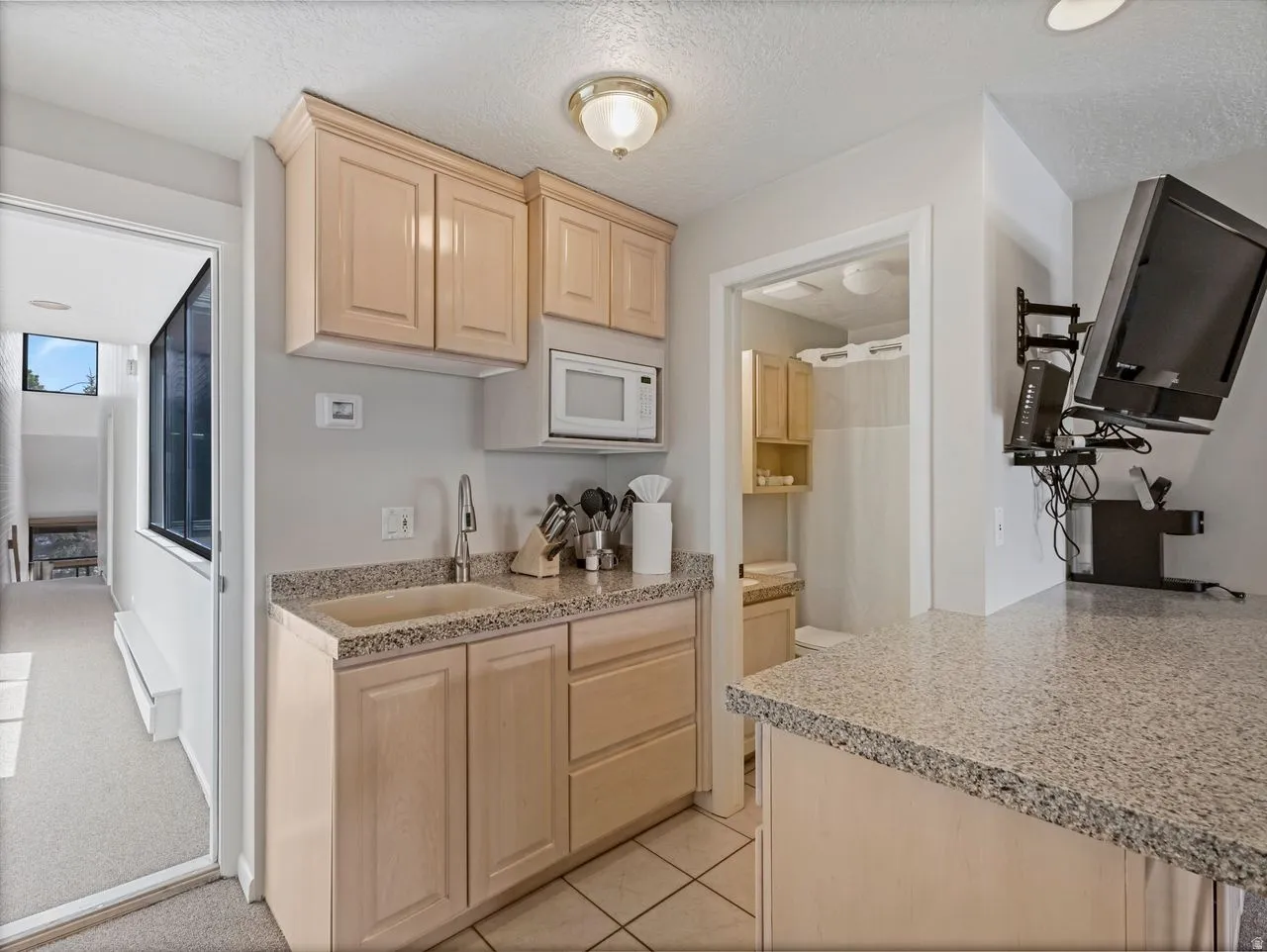 Kitchen featuring light wood finish cabinetry, a textured ceiling, white microwave, a baseboard radiator, and light tile patterned flooring