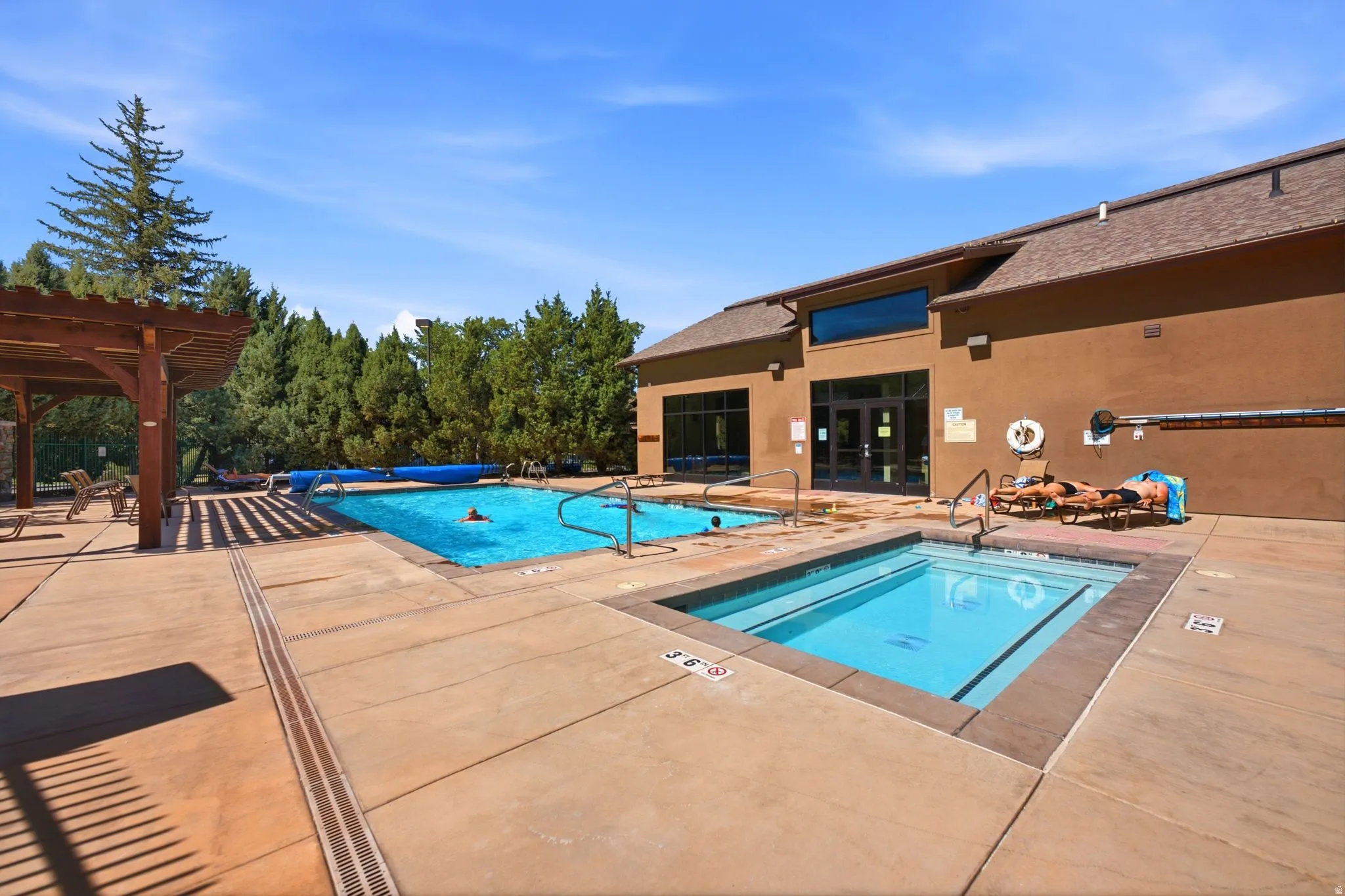 Outdoor swimming pool with integrated spa, expansive concrete decking, and adjacent clubhouse building