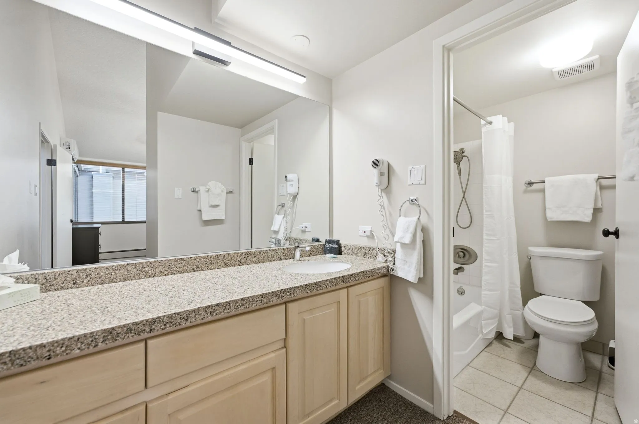 Bathroom featuring a light-toned vanity with a speckled countertop, an integrated sink, and an expansive mirror