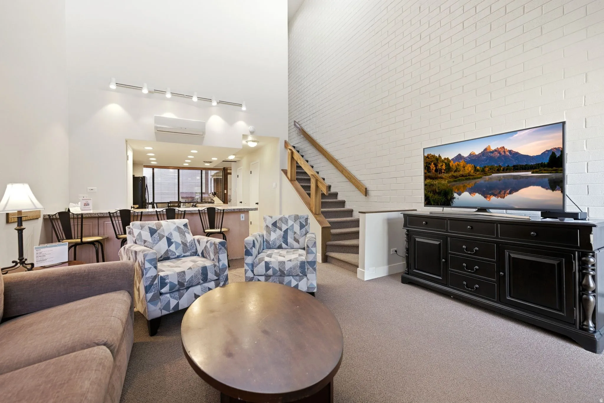 Two-story living area featuring a brick accent wall, track lighting, and a built-in breakfast bar with seating