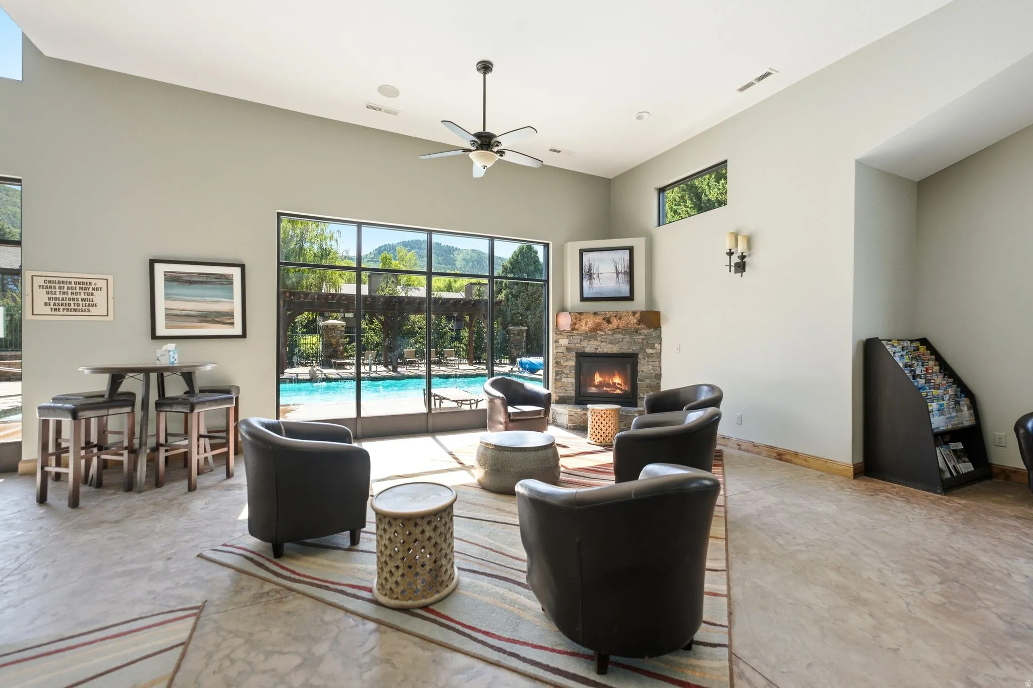 Spacious room featuring floor-to-ceiling windows, a stone-surround fireplace, and a high vaulted ceiling with a ceiling fan