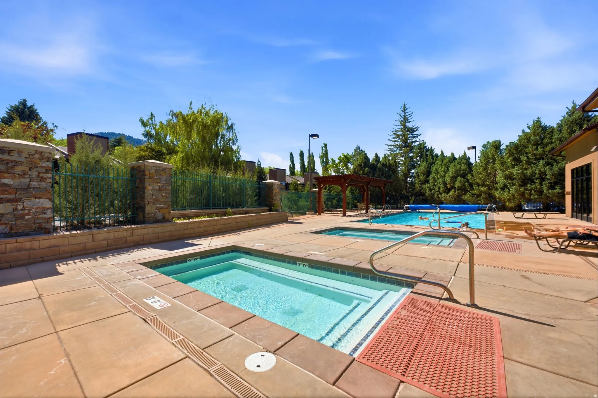 Outdoor pool area featuring two distinct spas, a swimming pool with a partial cover, and a wooden pergola structure