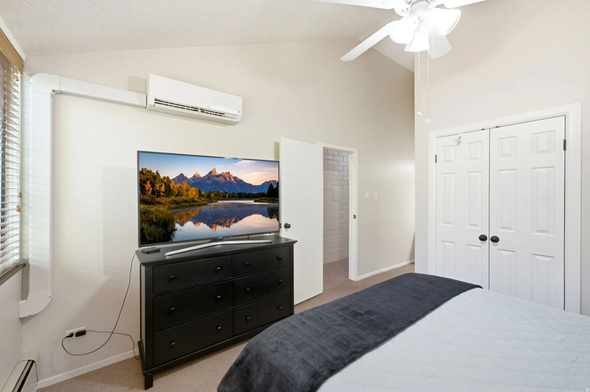 Vaulted ceiling room featuring a ceiling fan, mini-split air conditioning unit, and white bi-fold closet doors