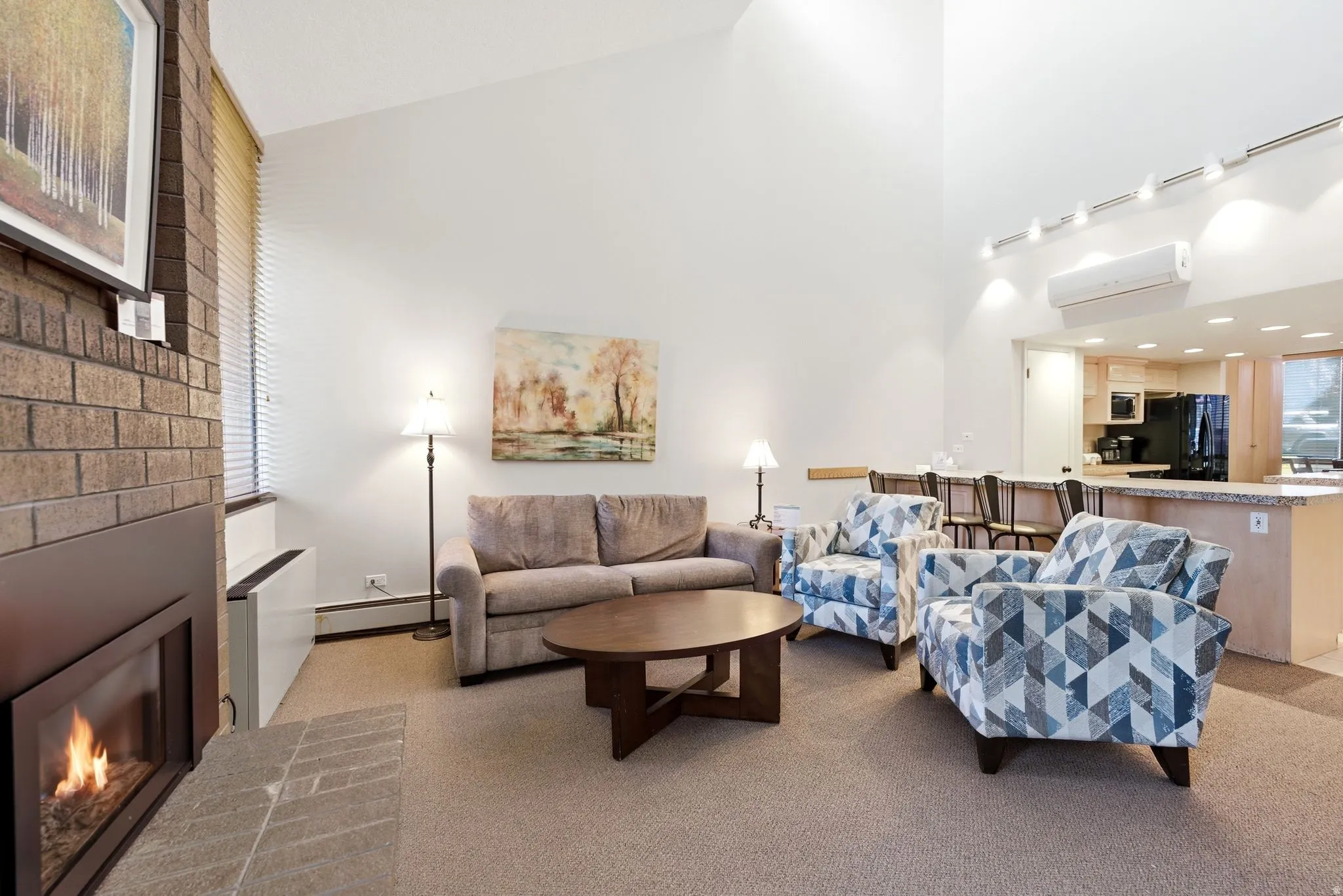 Vaulted ceilings enhance this living area featuring a brick fireplace, track lighting, and carpet flooring
