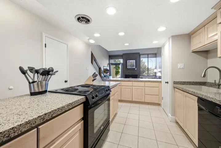 Kitchen featuring light wood-finish cabinetry, granite-style countertops, tile flooring, a black electric range, and a black dishwasher
