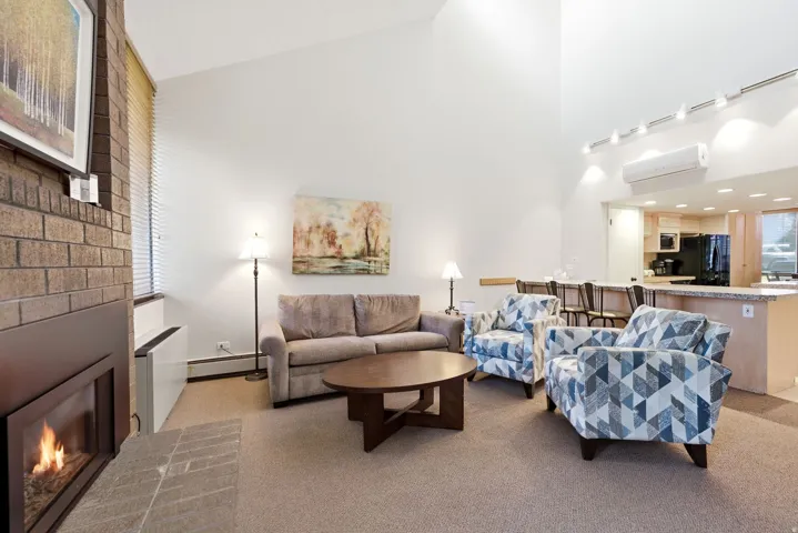 Vaulted ceilings enhance this living area featuring a brick fireplace, track lighting, and carpet flooring