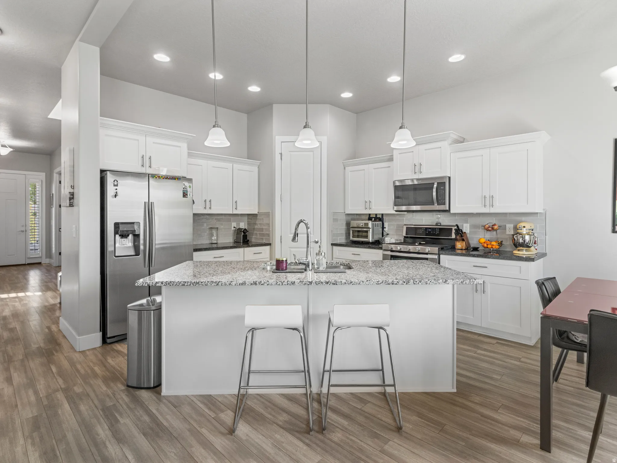 Kitchen featuring stainless steel appliances, white cabinets, an island with sink, a breakfast bar, and decorative light fixtures