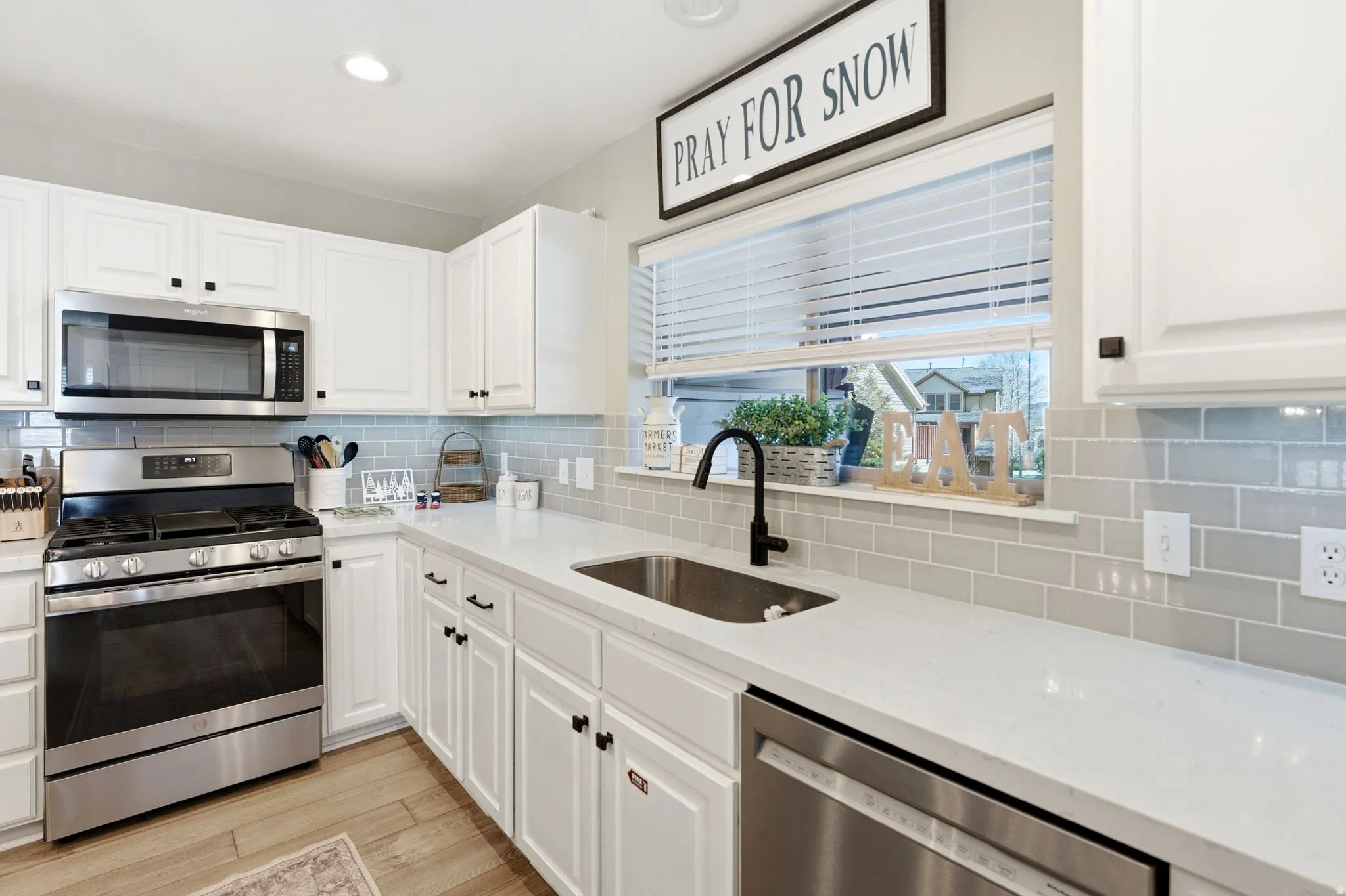 Kitchen with stainless steel appliances, light stone countertops, white cabinets, light wood-style flooring, and backsplash