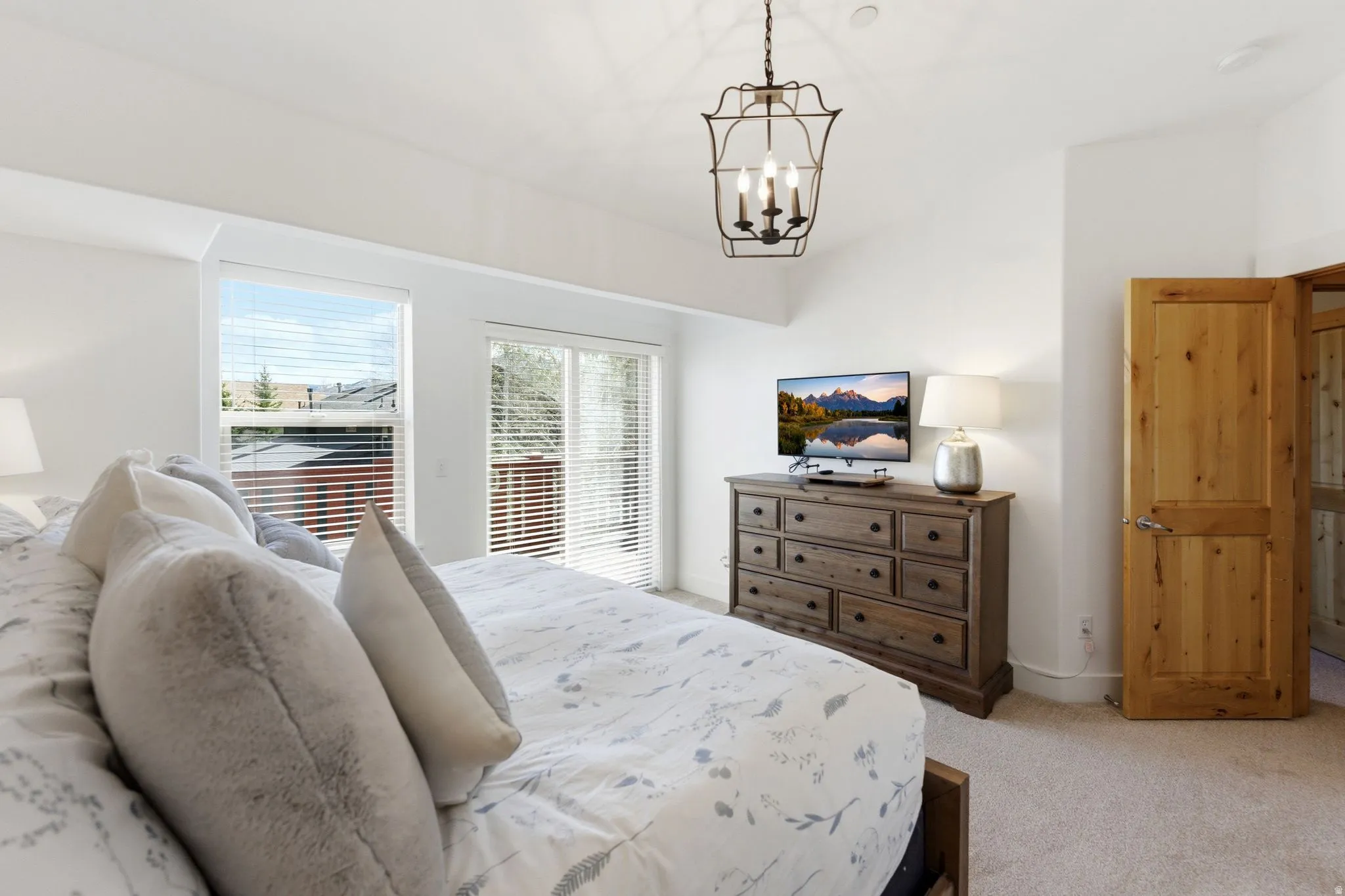 Bedroom with light carpet, hanging lights, and access to exterior