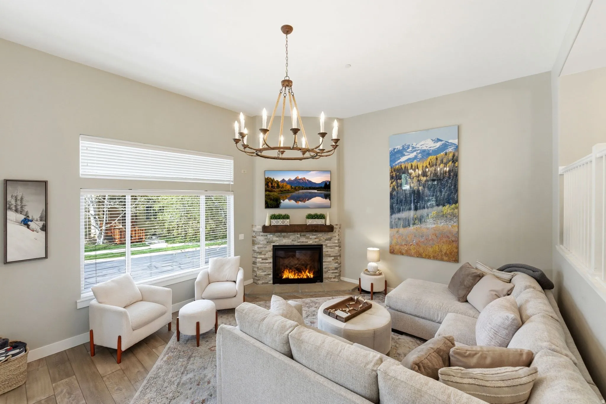 Living room with wood-type flooring, suspended lighting, and a stone fireplace